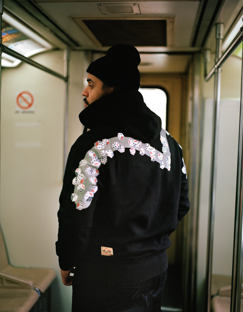 Person in a hoodie with a playing card design on the back, standing in a train car