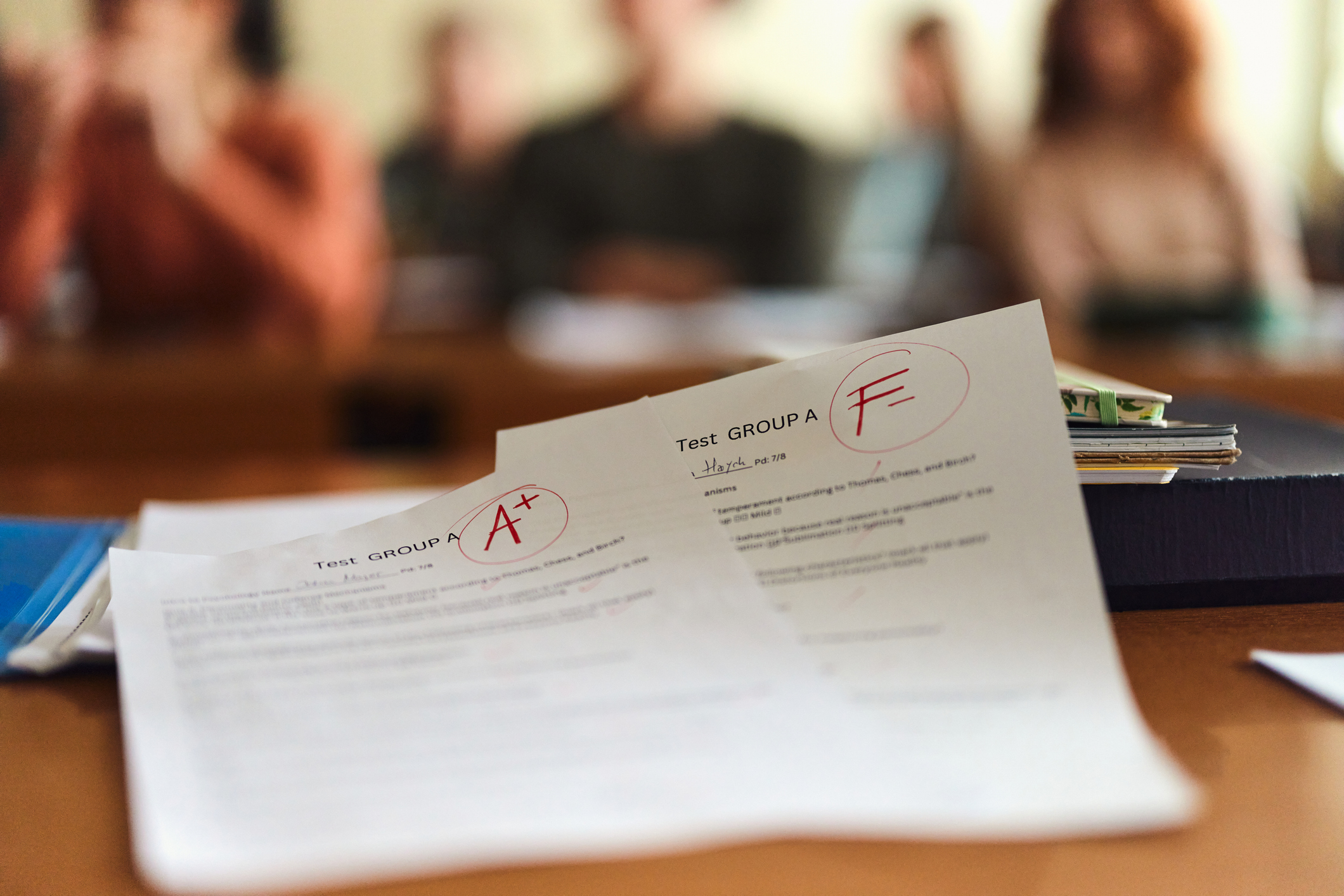 Papers on a desk with &quot;A+&quot; and &quot;F&quot; grades, students in the blurry background