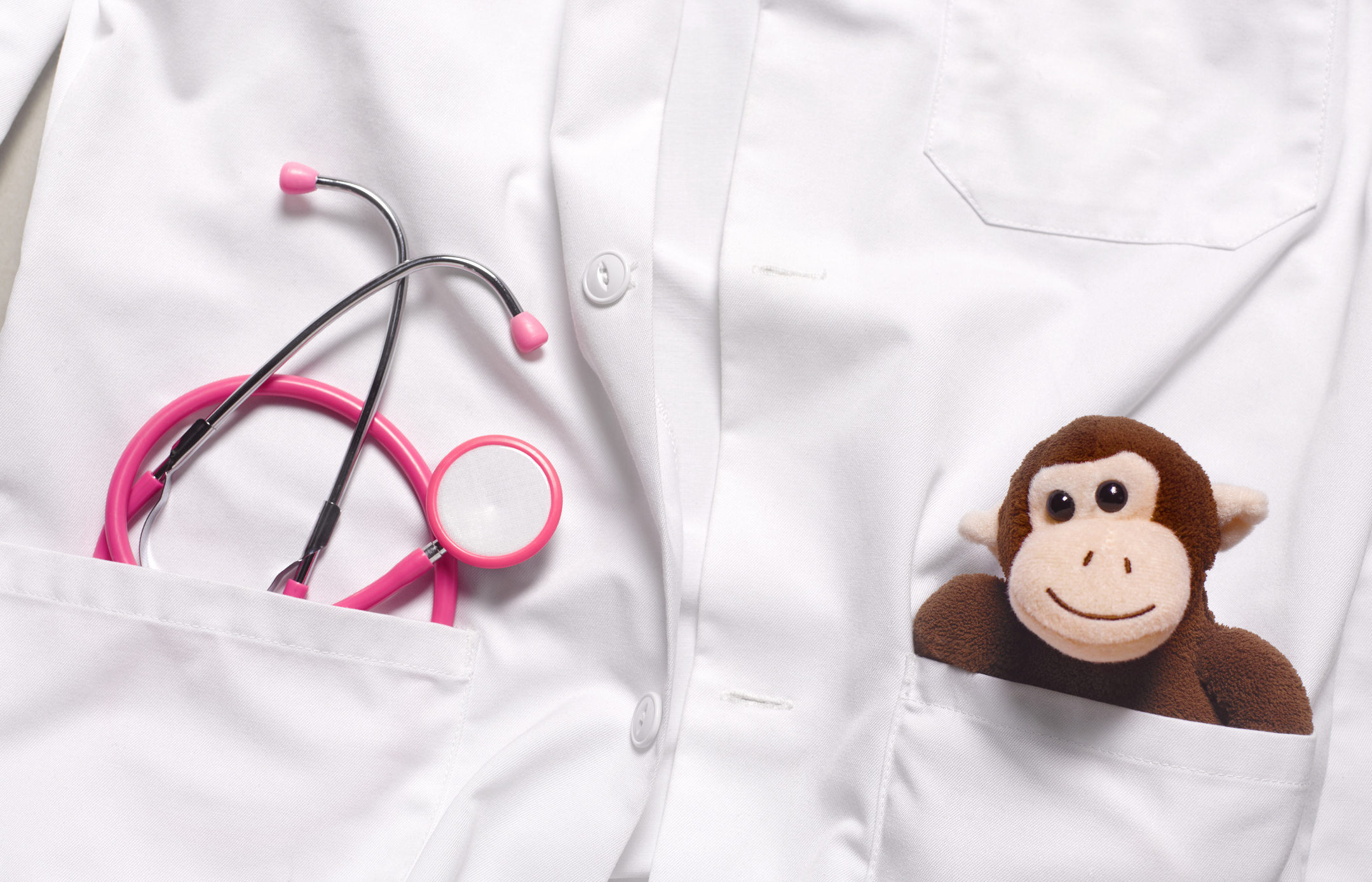 Close-up of a medical professional&#x27;s white coat with a stethoscope and a plush monkey in the pocket, suggesting pediatric care