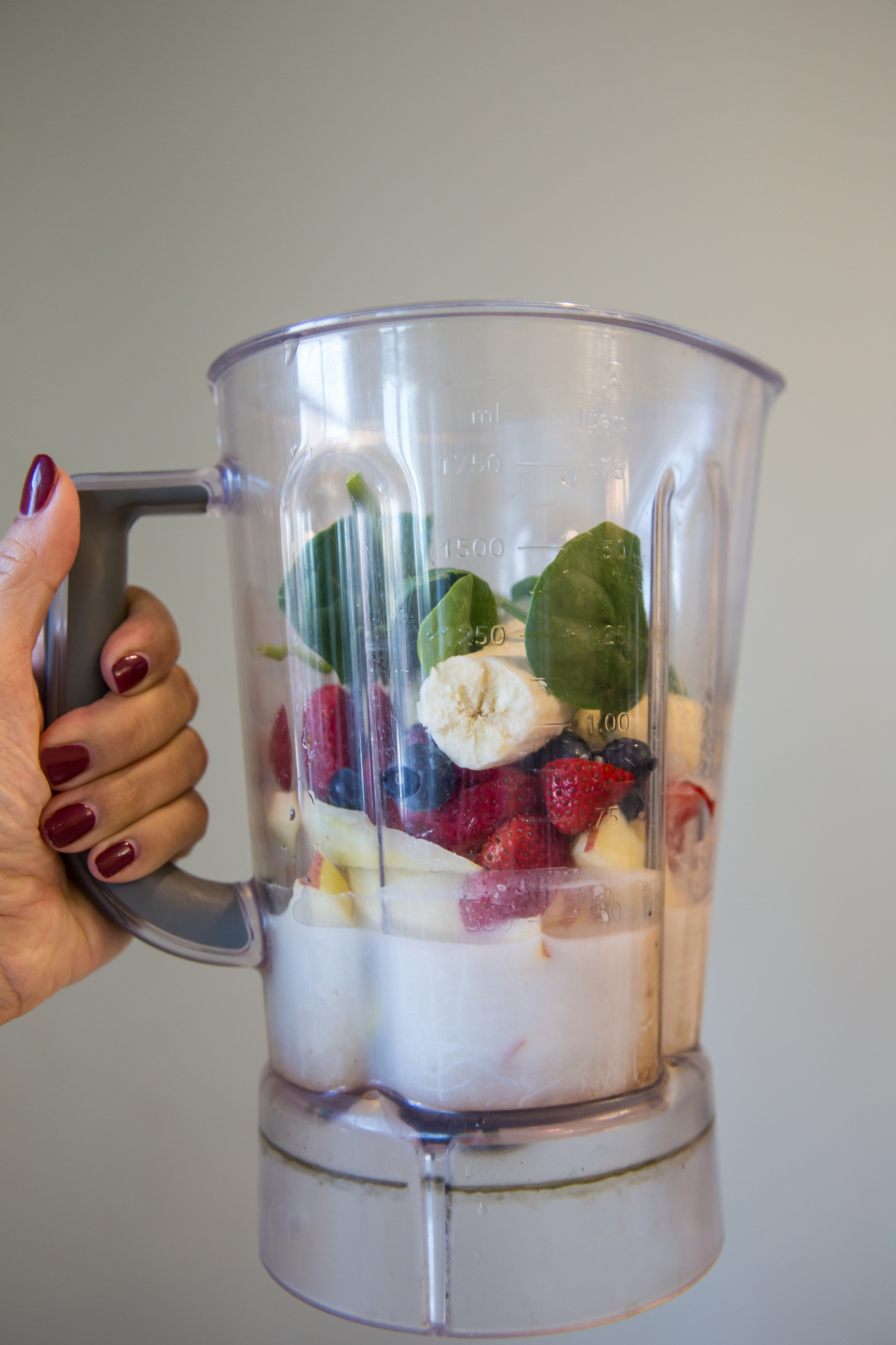 Hand holding a blender filled with assorted fruits and spinach, ready to blend