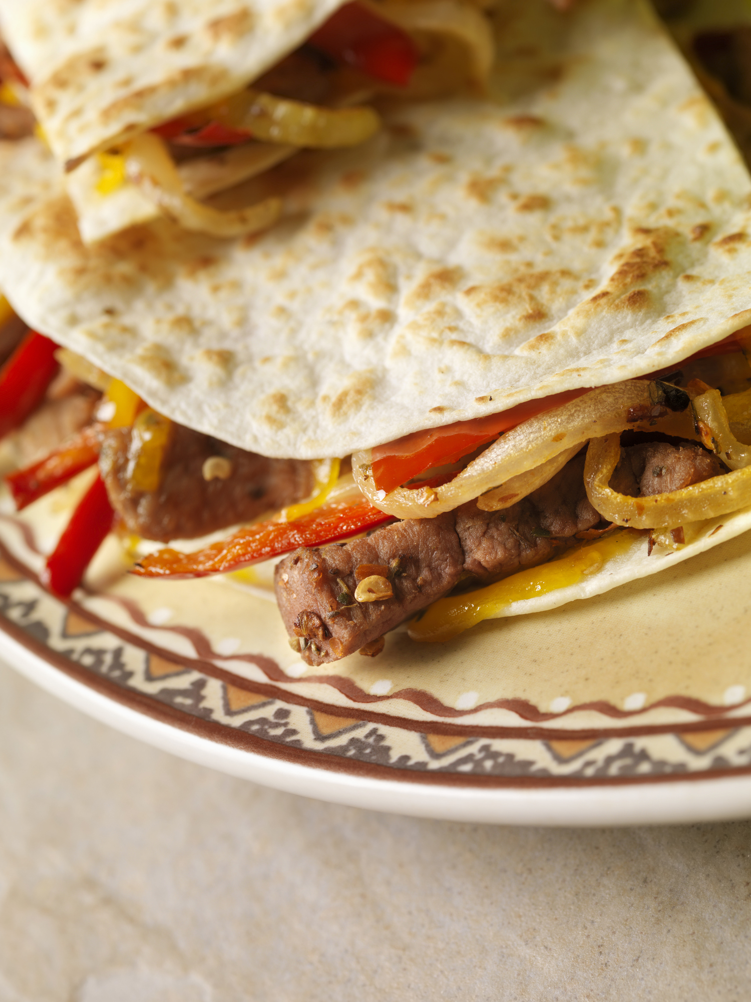 Close-up of a quesadilla filled with cheese, beef, and bell peppers on a decorated plate