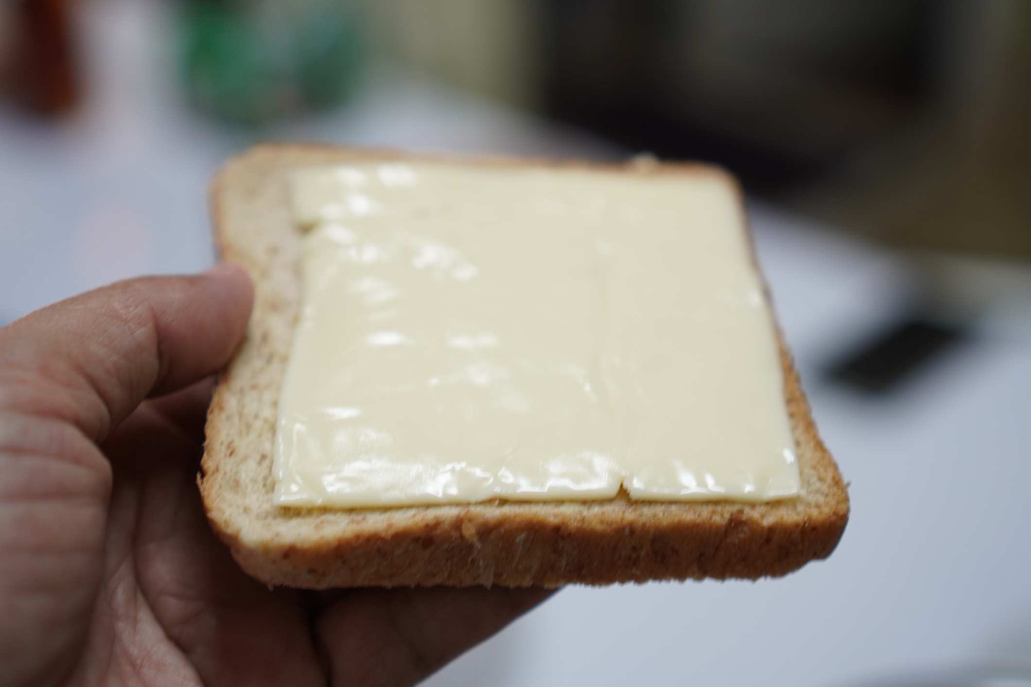 Hand holding a slice of bread with a spread, possibly butter or cheese