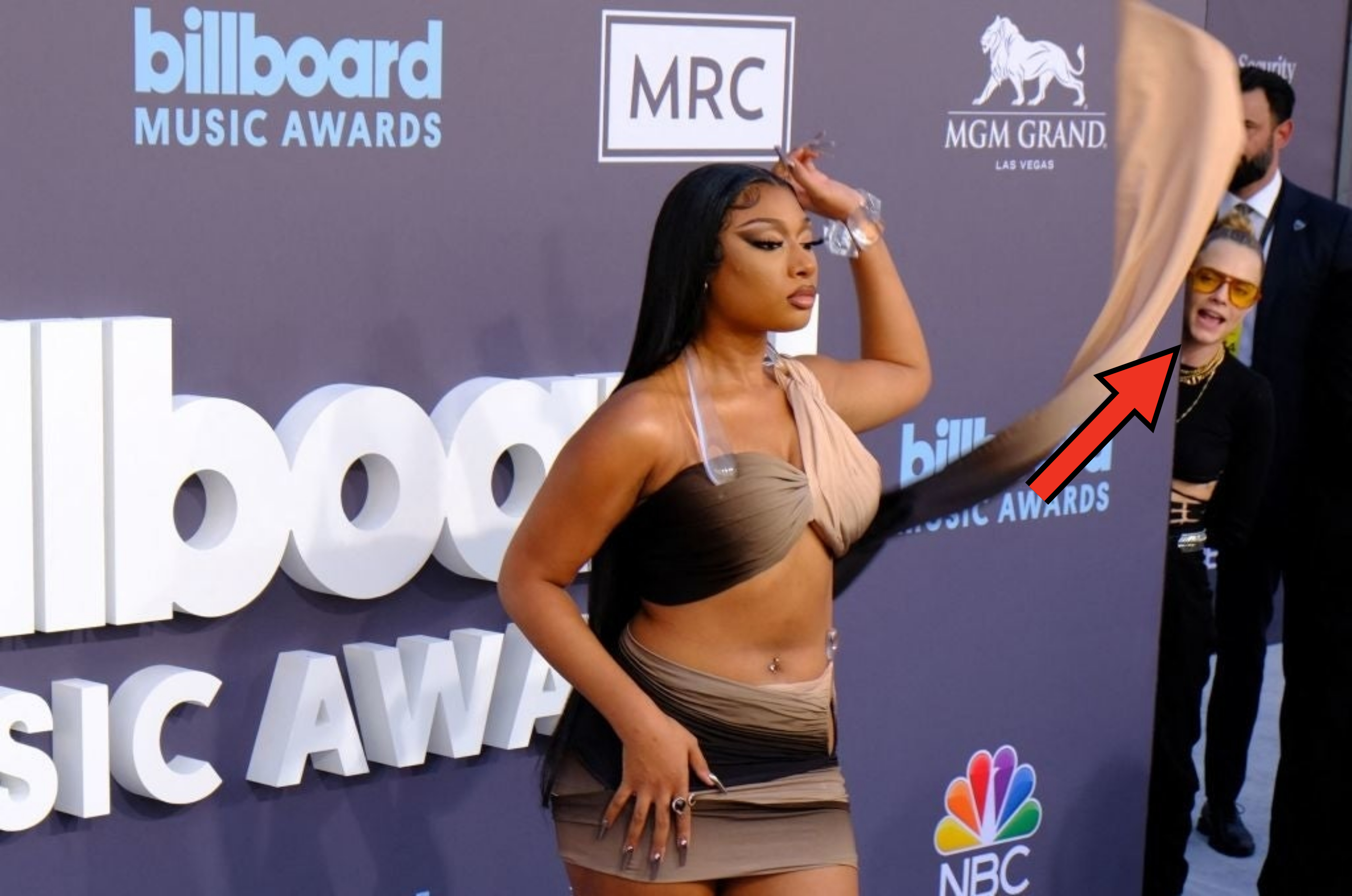 Megan Thee Stallion poses in a stylish asymmetrical dress at the Billboard Music Awards, with cara hiding behind her