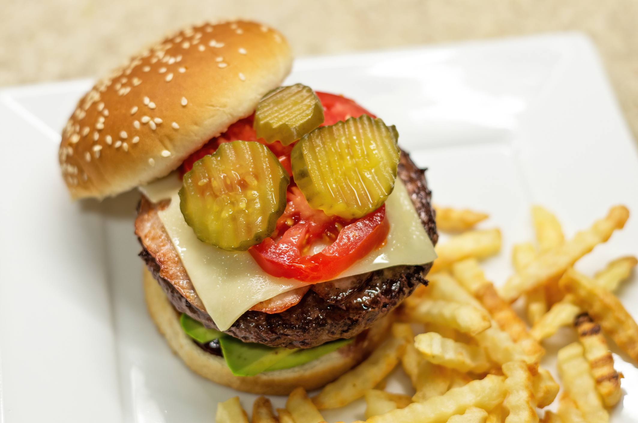 Cheeseburger with pickles, tomato, lettuce, patty on a plate with fries on the side