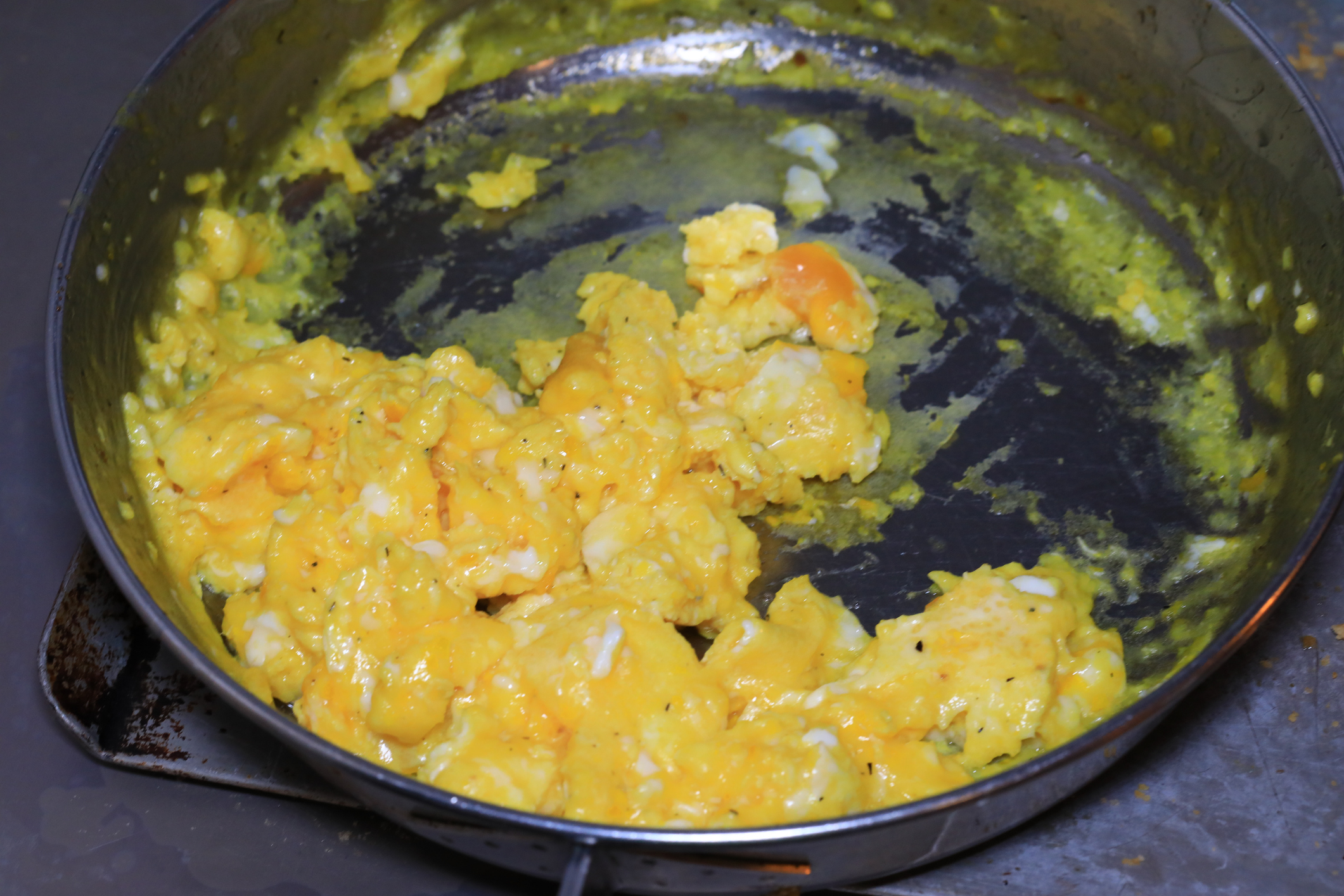 Scrambled eggs in a black skillet with some sticking to the pan