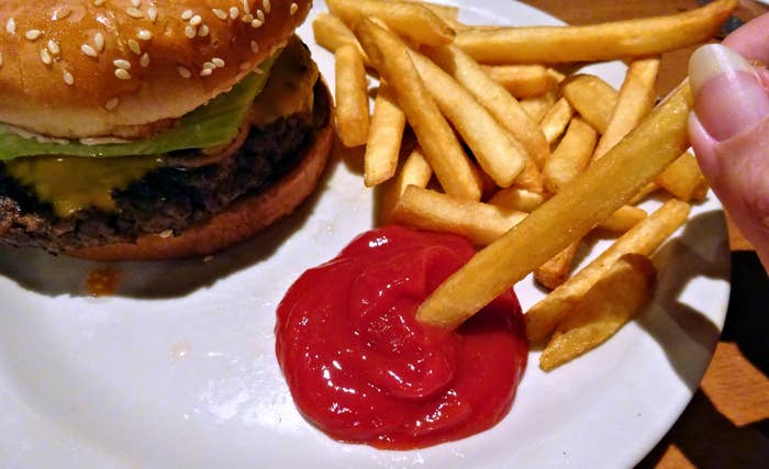 A person dipping a fry into ketchup with a burger on the side