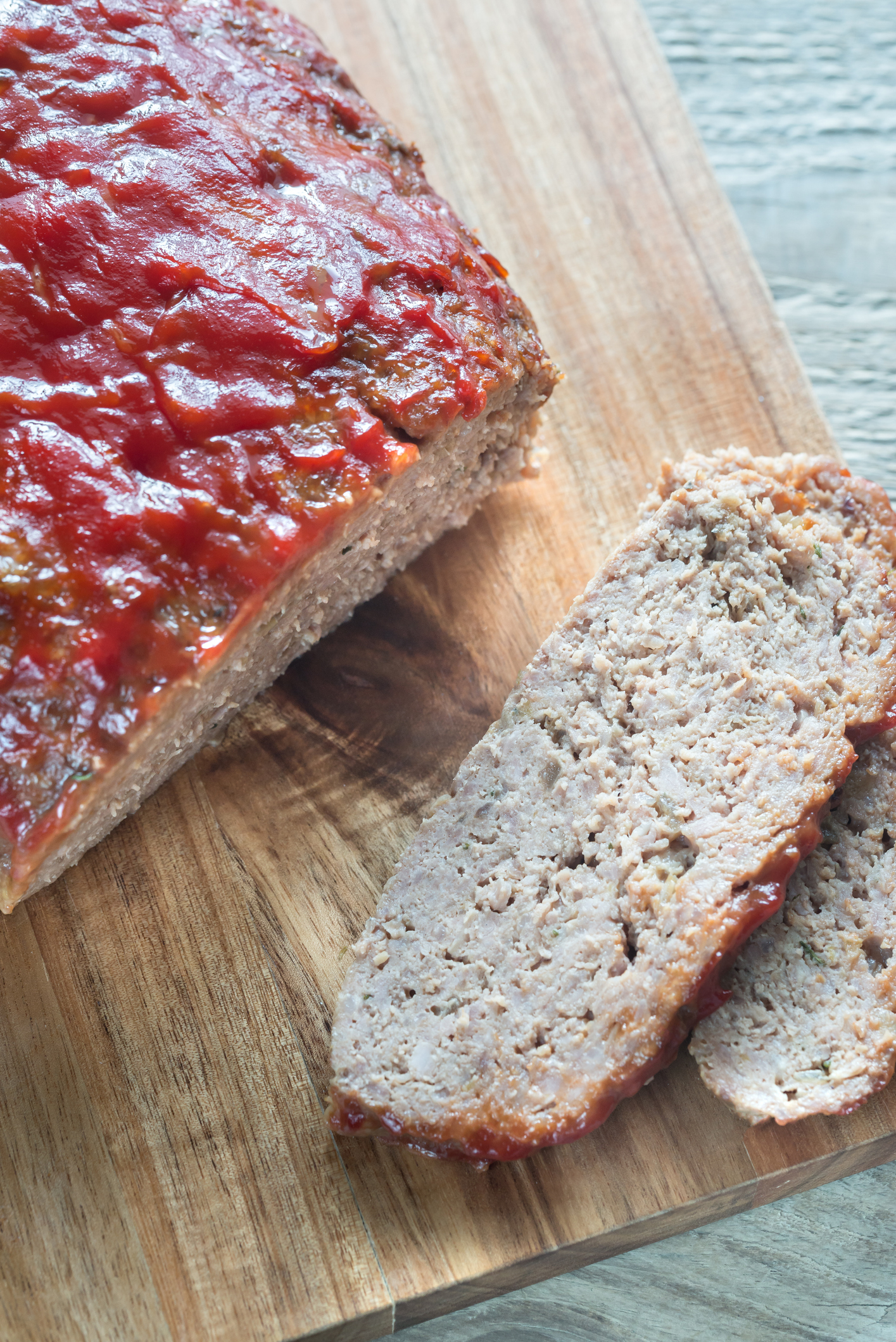Sliced meatloaf on a wooden board with one piece cut