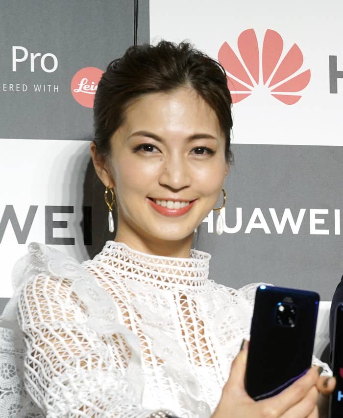 女性が白いドレスを着て、イベントでカメラを持ち笑顔で写真を撮っています。