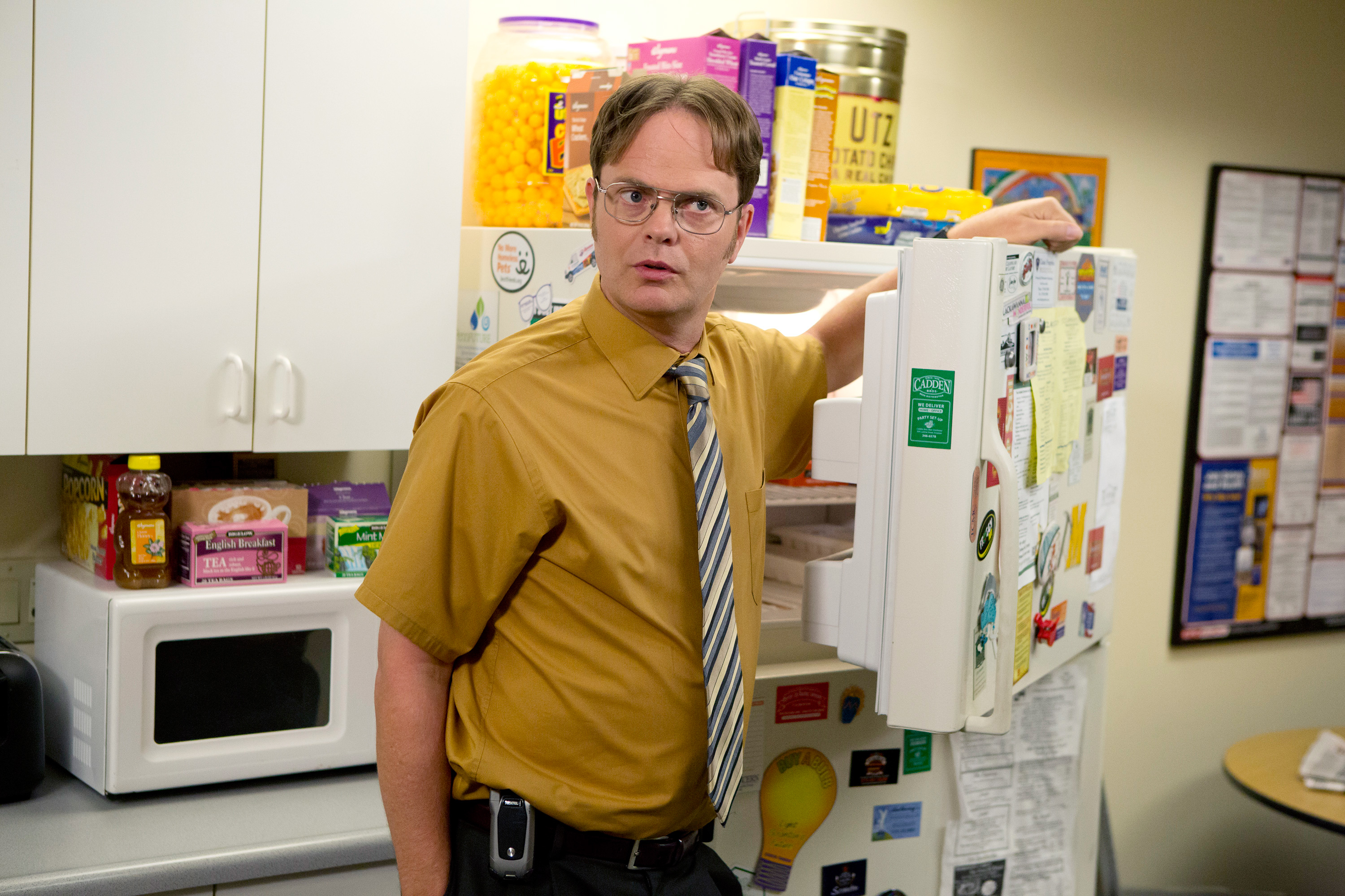Man as TV character Dwight from &quot;The Office&quot; standing by an open fridge in an office kitchen
