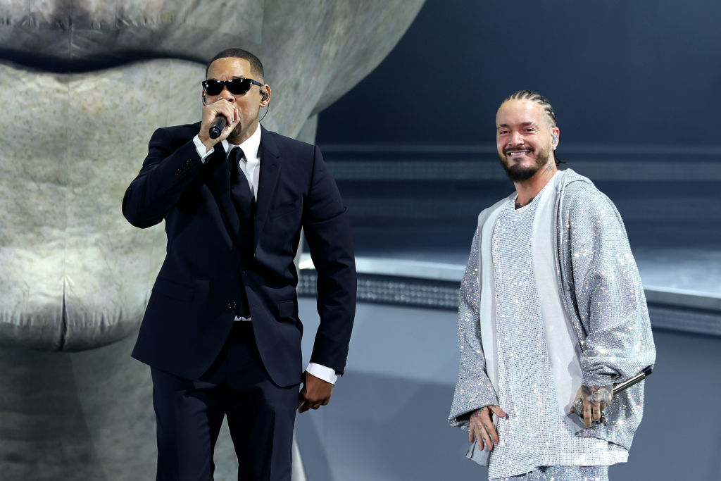 Jay-Z in a suit speaking into a microphone; Post Malone beside him in a sparkly outfit. They&#x27;re on stage with a giant sculpture backdrop