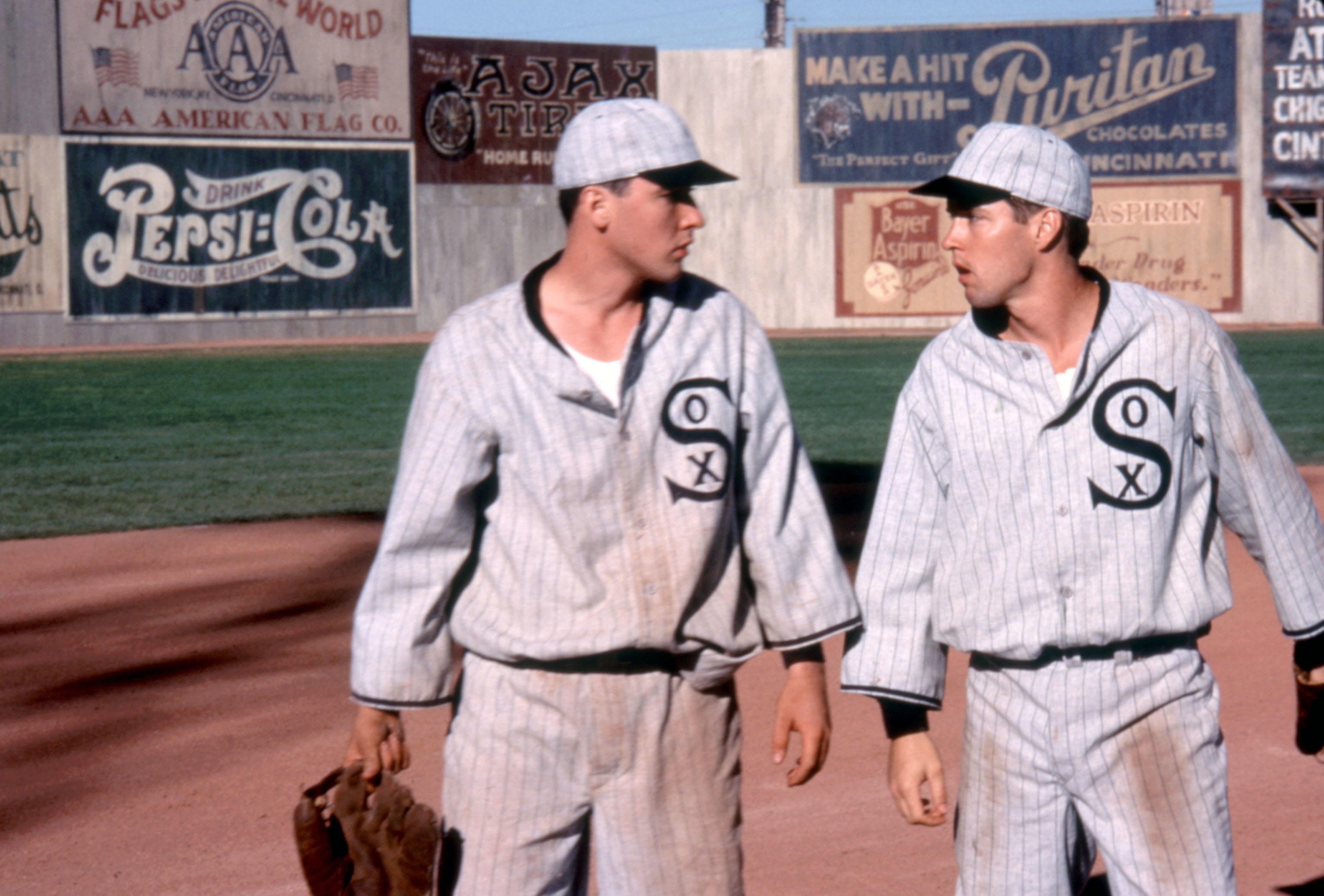 Two baseball players in vintage Chicago White Sox uniforms converse on the field