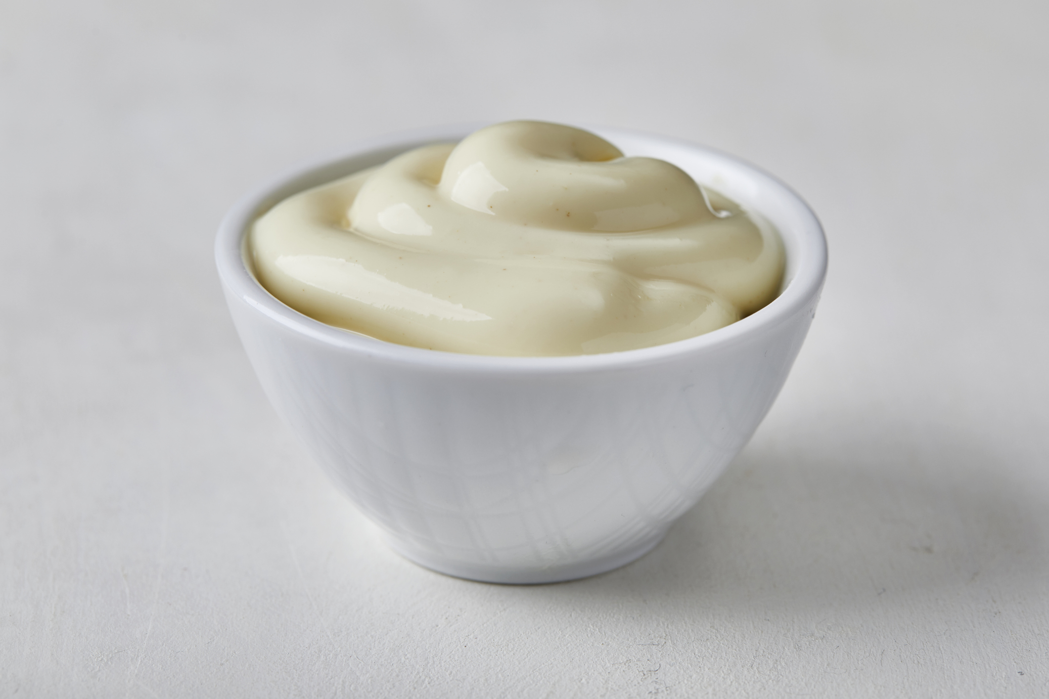 A bowl of mayonnaise on a plain surface