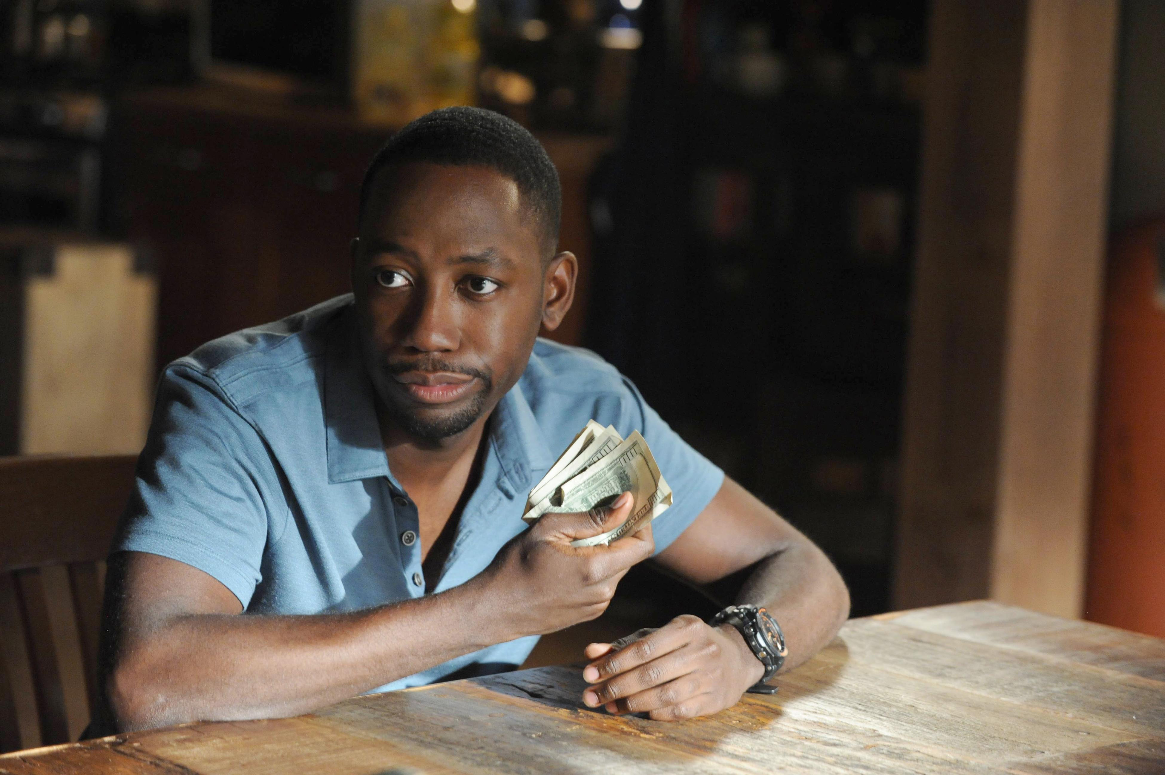 Man at table with contemplative expression holding money, in a scene likely from a TV show or movie
