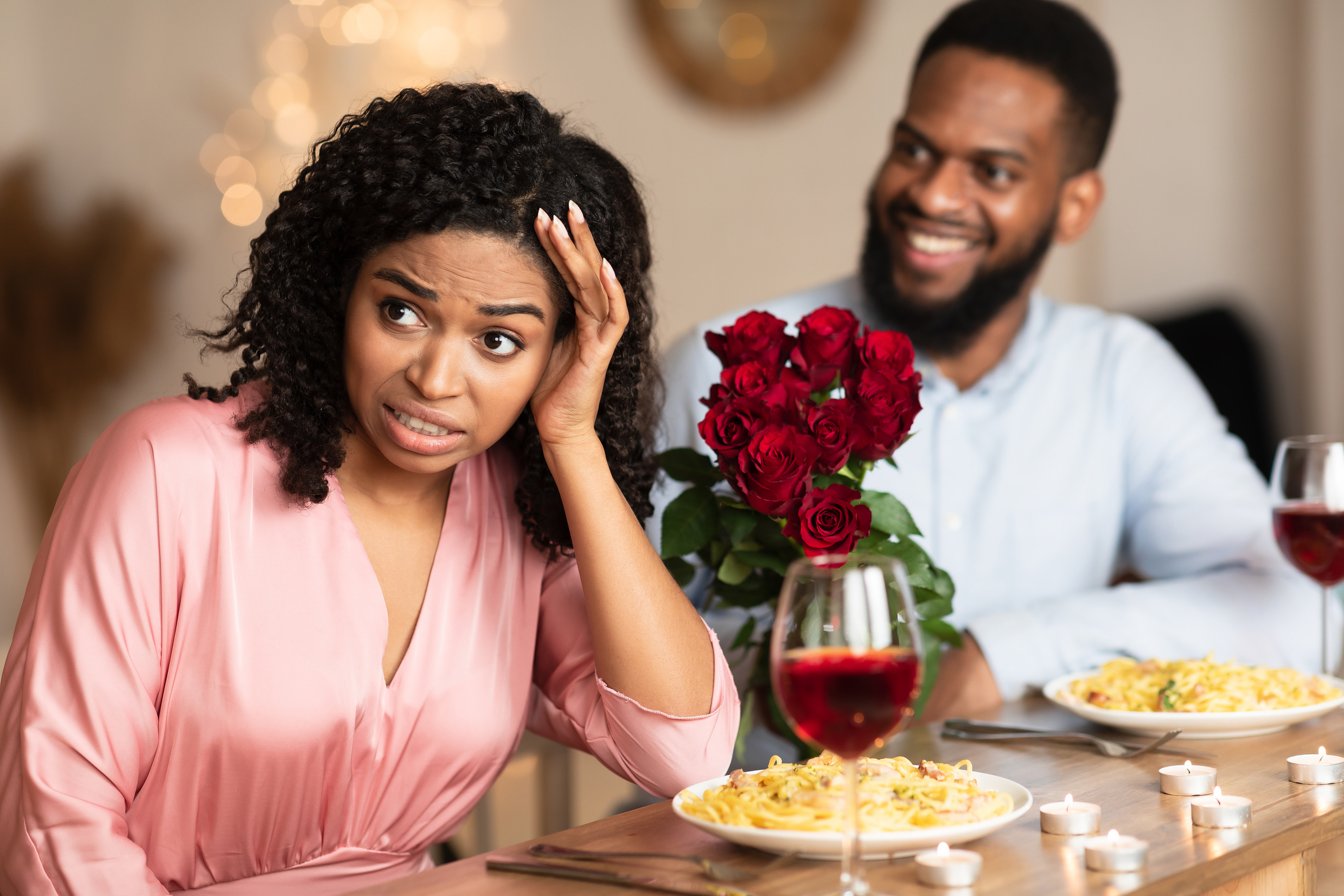 Woman appears uncomfortable on date with amused man, bouquet on table, restaurant setting