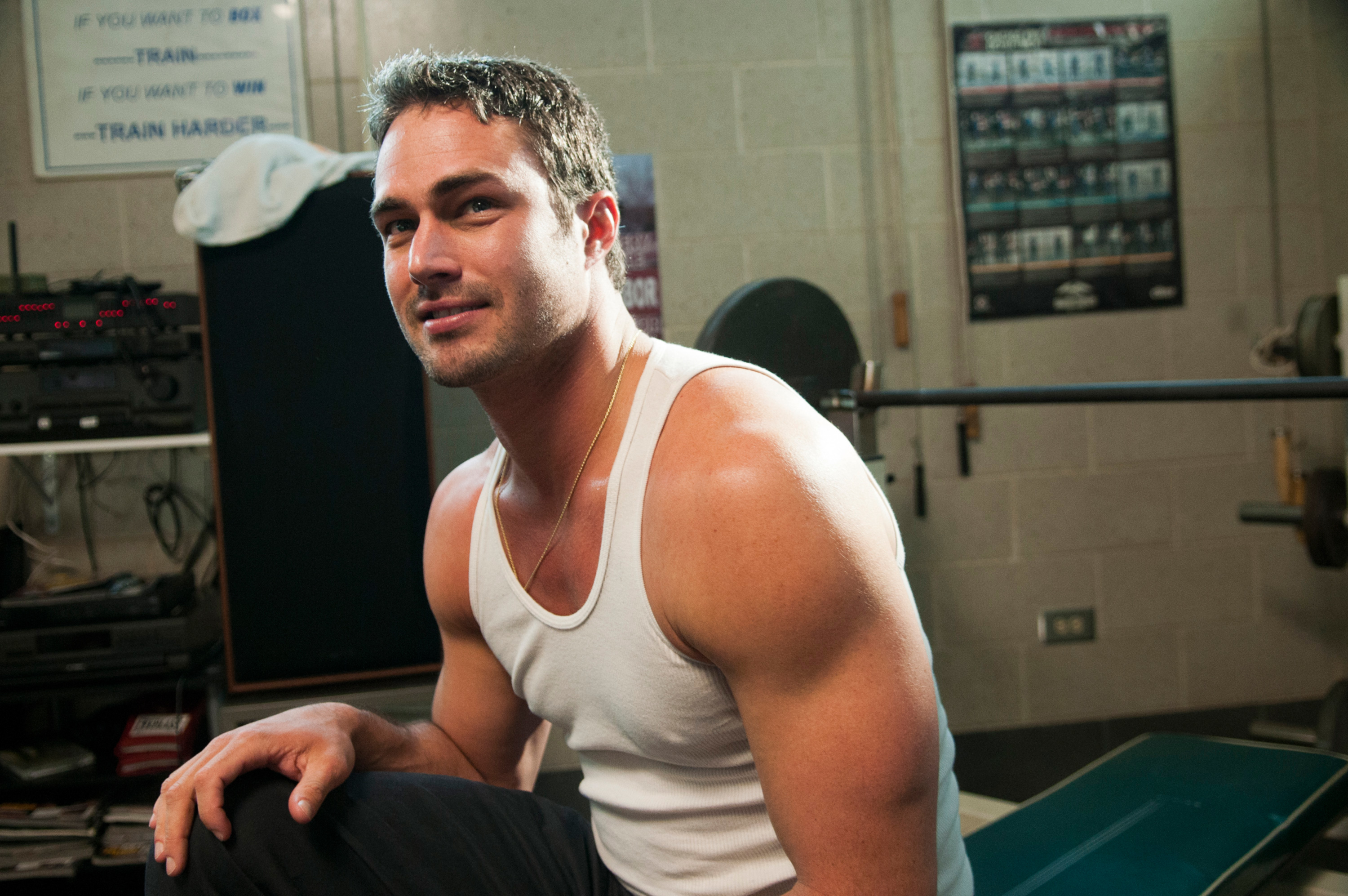 Man in a white tank top sitting in a gym, looking at the camera