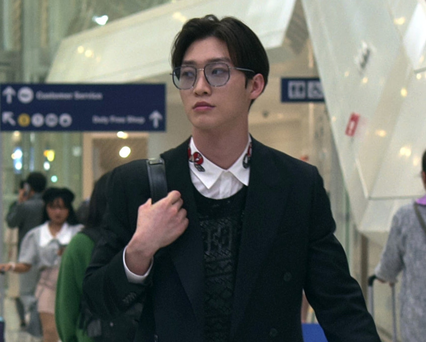 Man in a suit and glasses carrying a bag walks through an airport