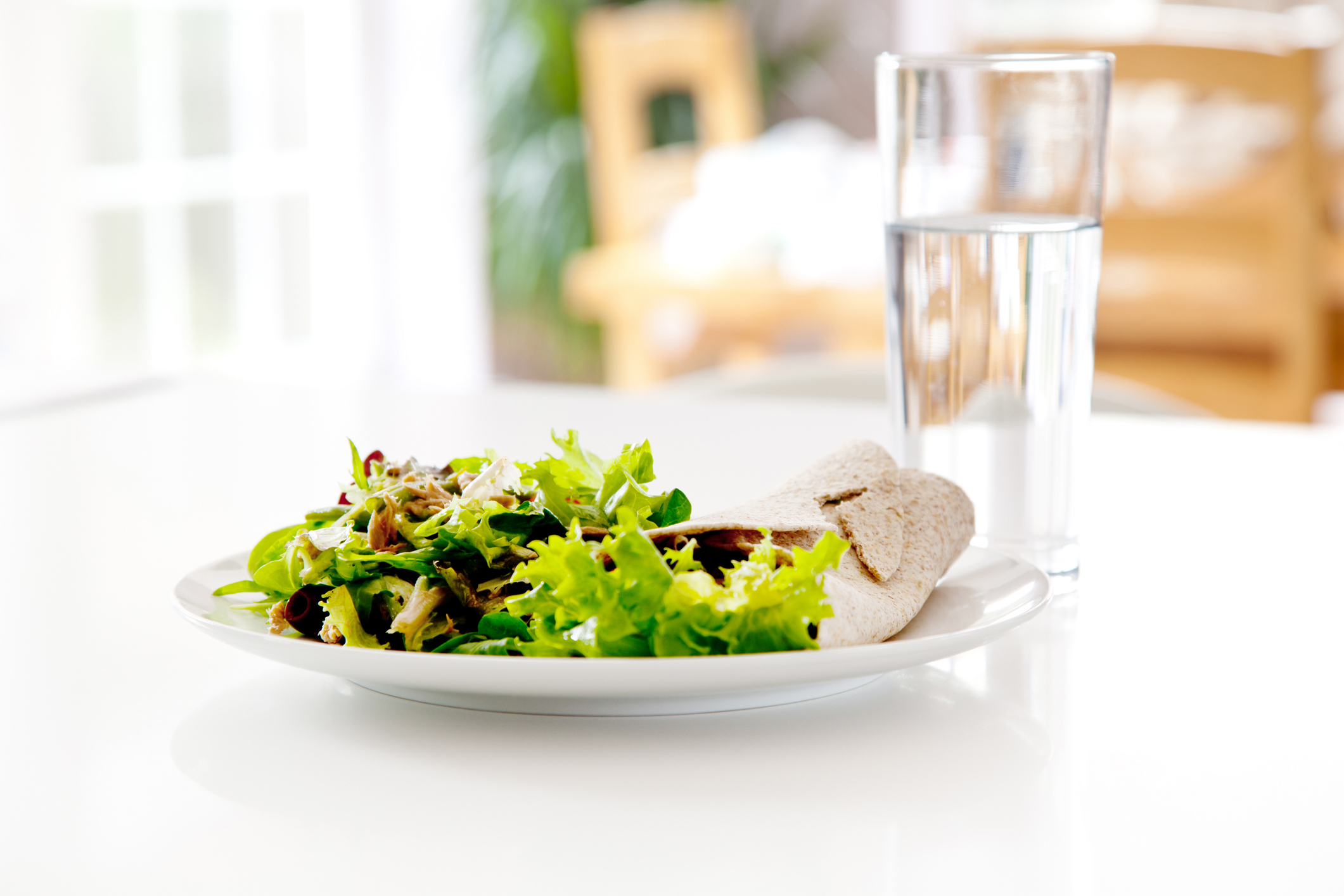 Salad plate with bread beside a glass of water on a table, implying a healthy meal for two