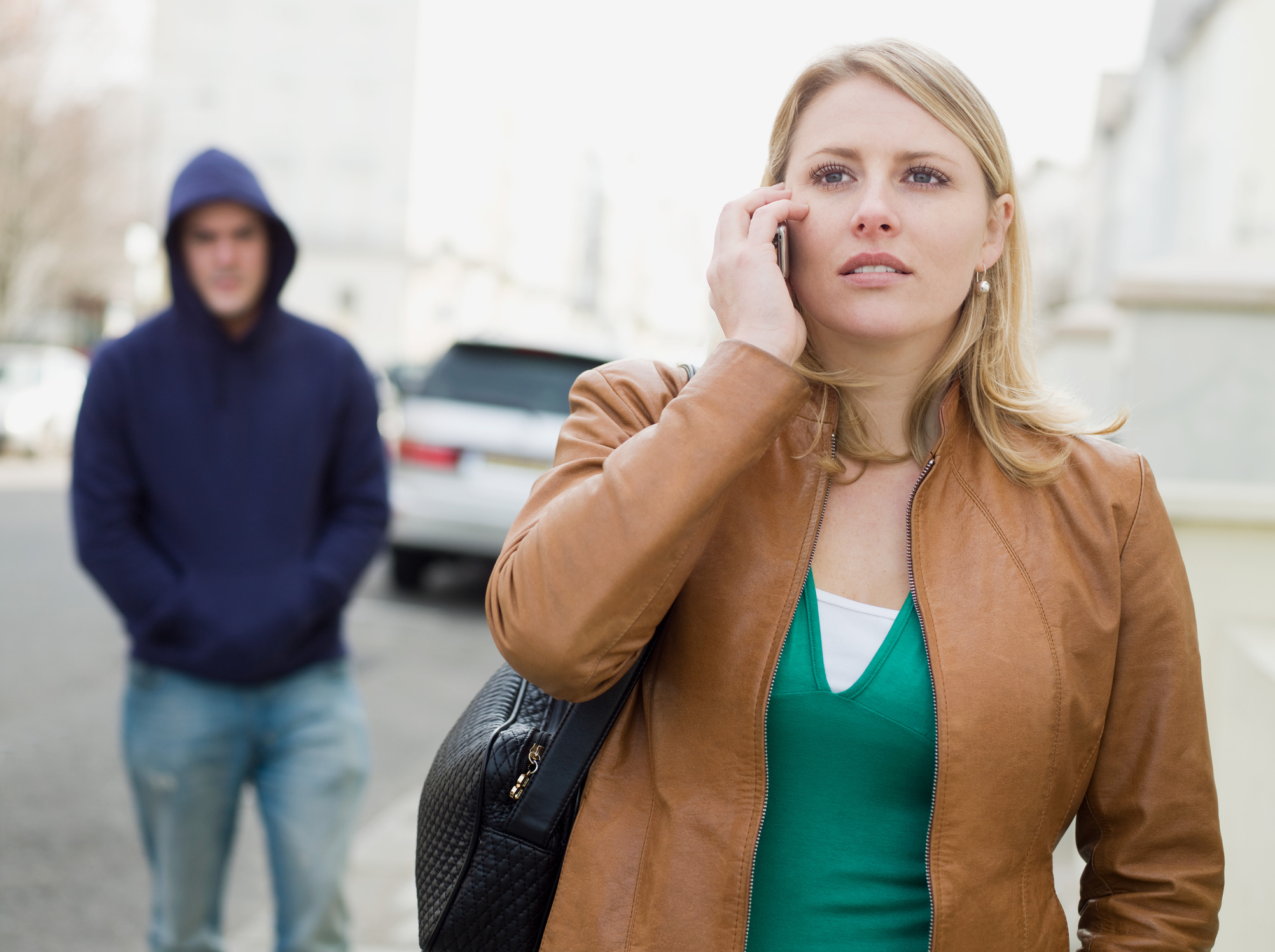 Woman on phone appears uneasy with a hooded figure in the background