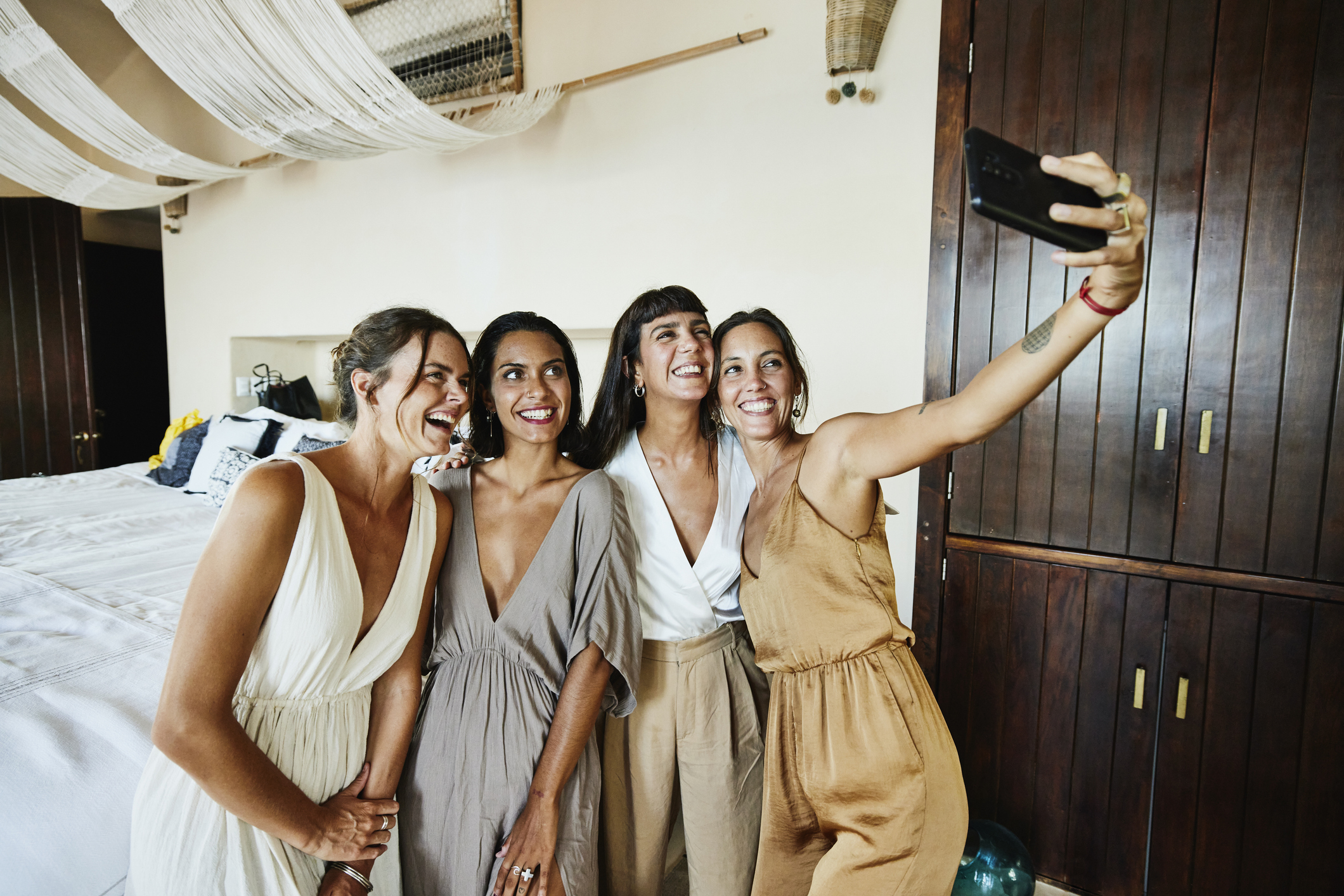 Four women in casual attire are smiling and taking a selfie indoors