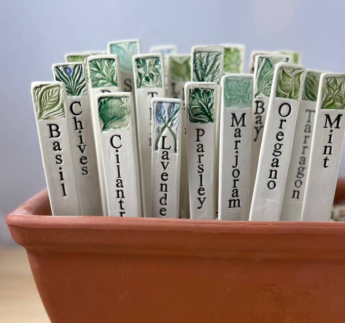 Ceramic herb markers with plant names in a terracotta pot, indicating different herbs for gardening