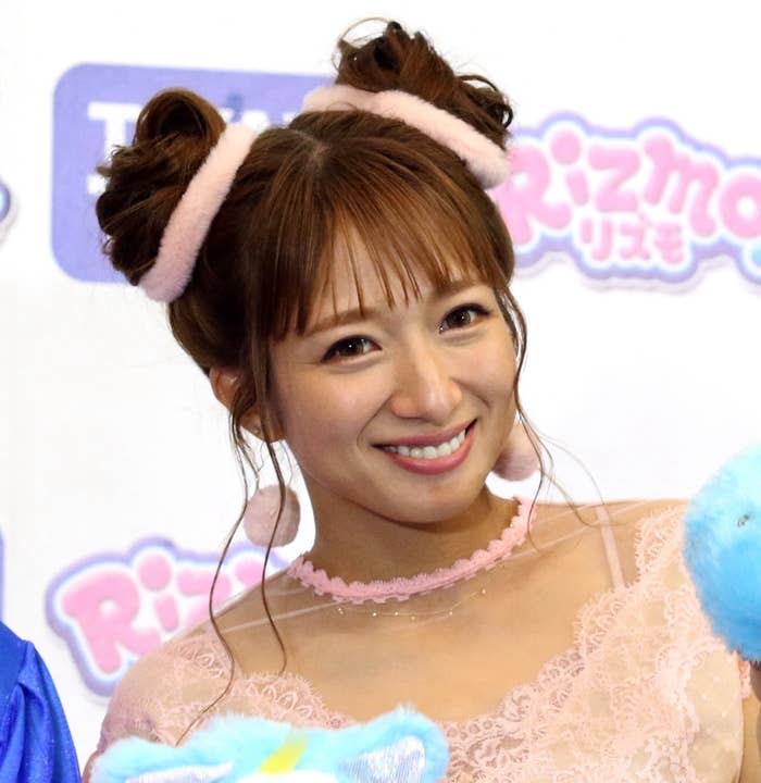 女性がピンクのドレスとヘアアクセサリーを付けて、カメラに向かって笑顔でポーズをとっています。