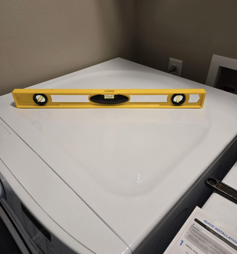 A yellow spirit level is centered on top of a white appliance, showing a balance reading