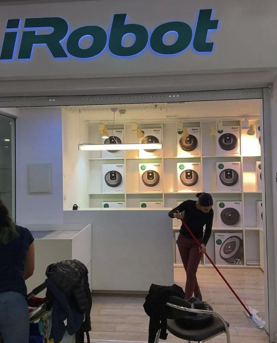 Person using a mop in front of an iRobot store with robot vacuums displayed