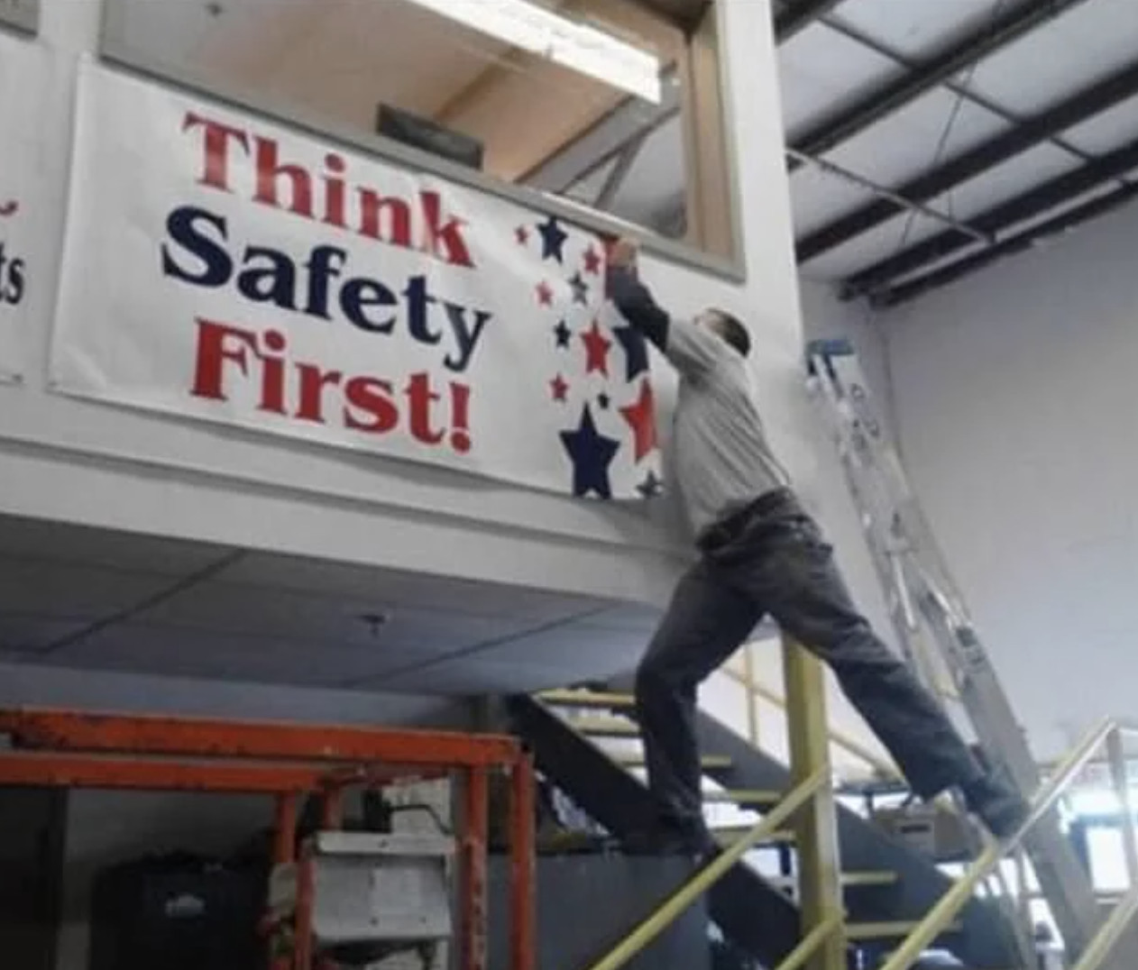 Person on top of a ladder reaching towards a &quot;Think Safety First!&quot; sign, unsafely balanced
