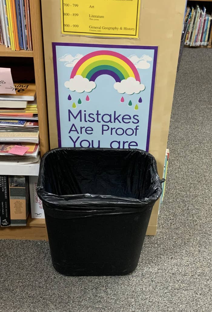 Sign reading &quot;Mistakes Are Proof You are Trying&quot; above a trash bin in a library by bookshelves