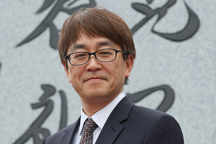 男性がスーツ姿で赤い花のリボンを付けている。