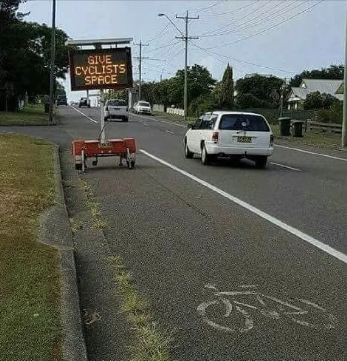 Electronic roadside sign reads &quot;GIVE CYCLISTS SPACE&quot; next to a bike lane with a car approaching