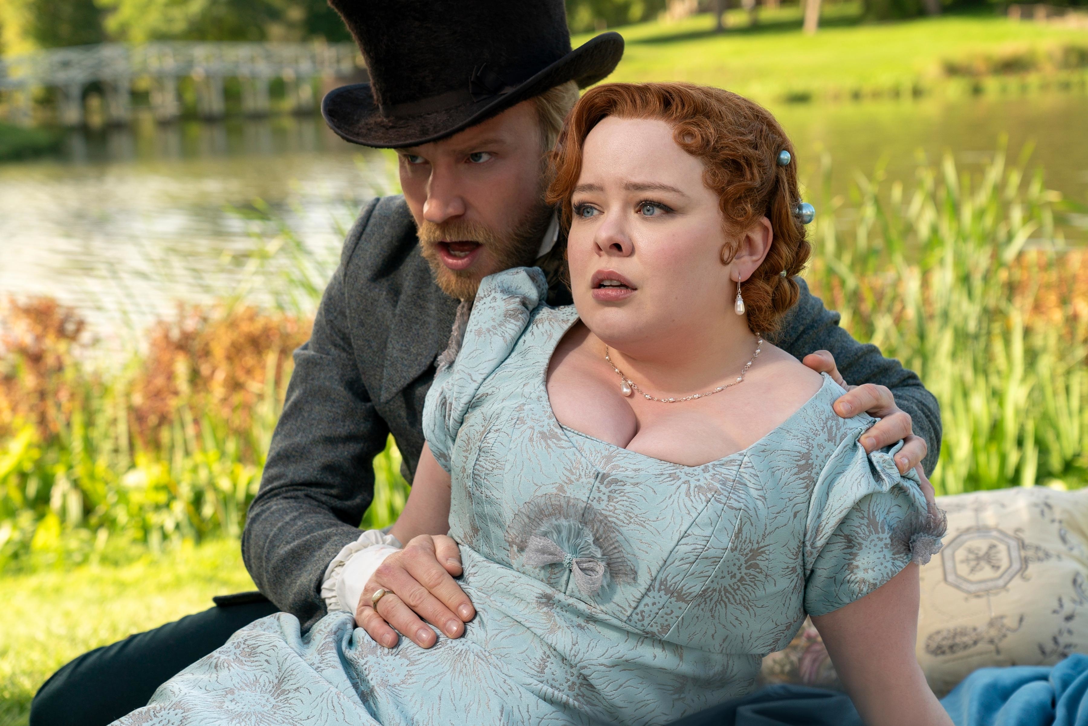 Two actors in period costume, the man in a top hat and the woman in a gown, engaged in a dramatic scene outdoors