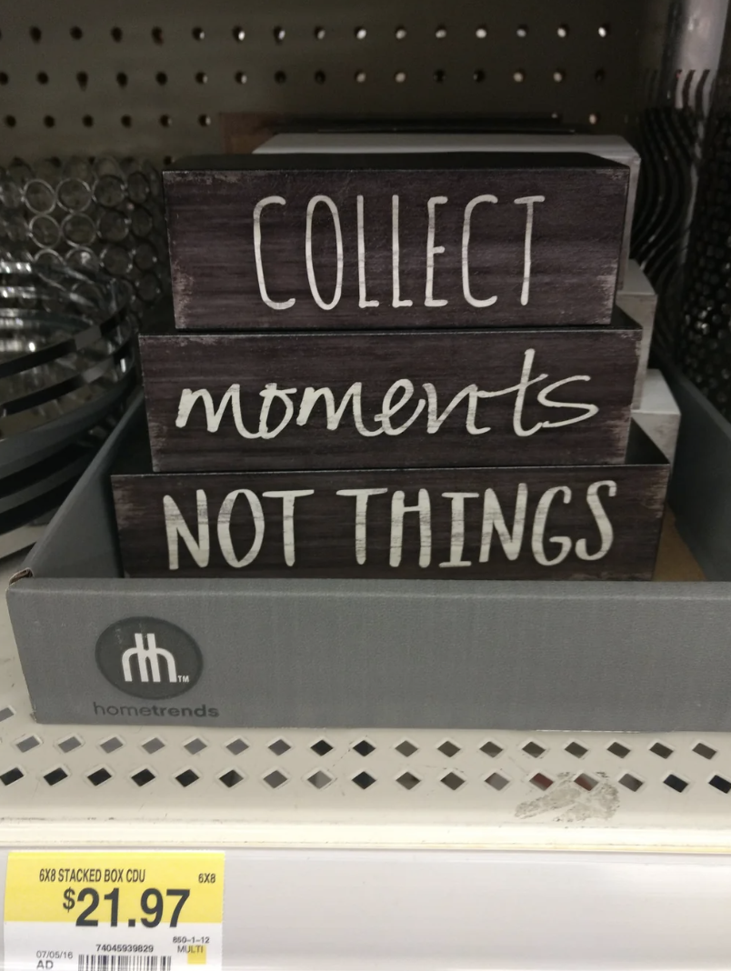 Decorative sign on a shelf stating &quot;COLLECT moments NOT THINGS&quot; with a price tag below