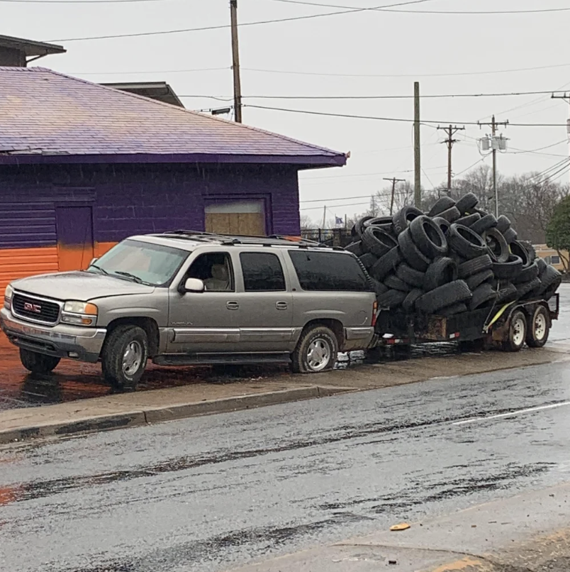 SUV pulling a trailer overloaded with tires on a wet street