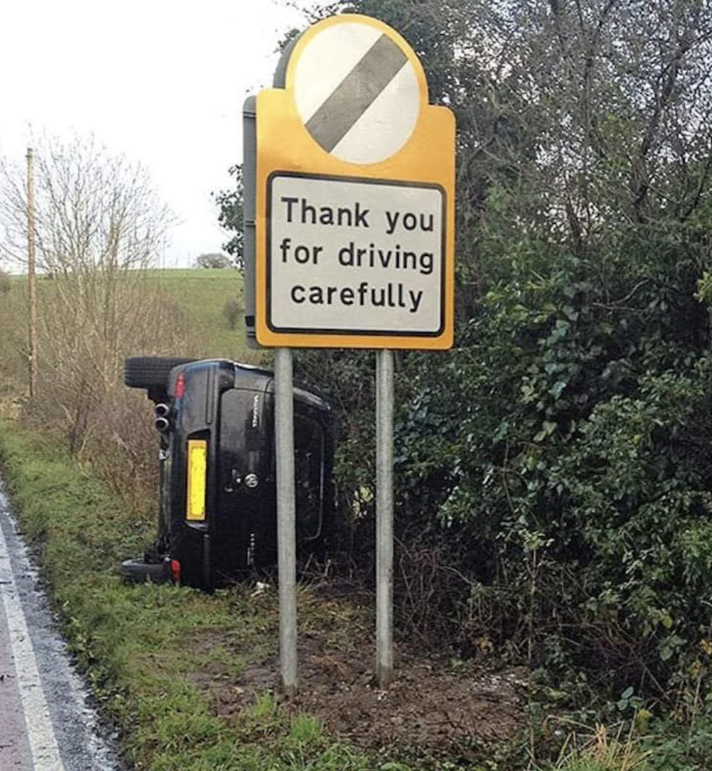 Sign reads &quot;Thank you for driving carefully&quot; next to an overturned car off the road