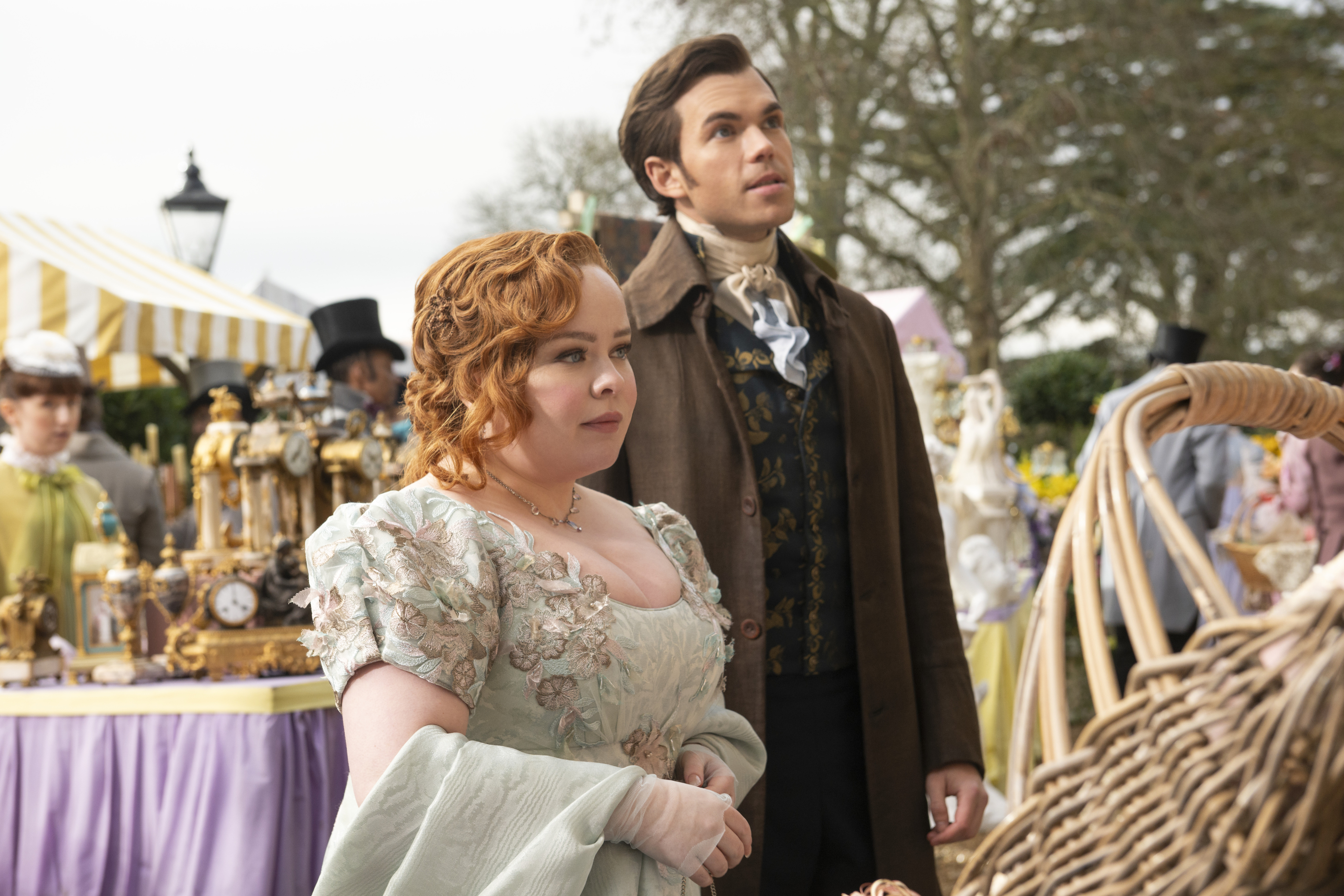 Penelope Featherington and Colin Bridgerton in historical attire at a daytime outdoor market