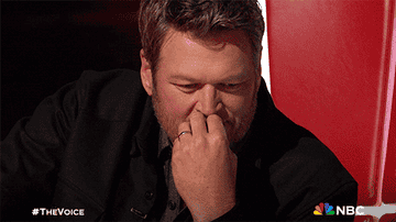 Blake Shelton presses his hand to his face in a pensive gesture as he sits in a "The Voice" judge's chair