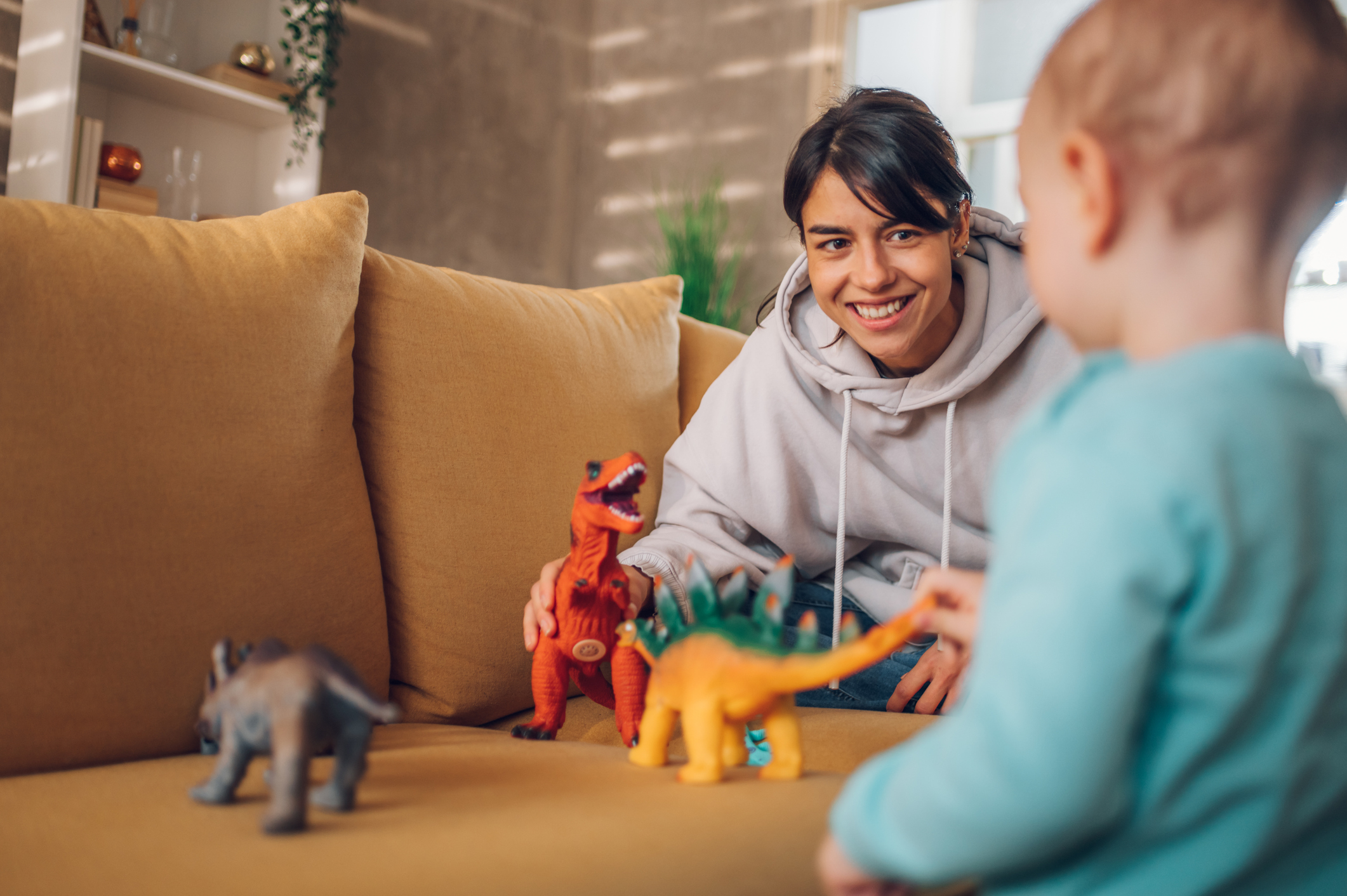 Adult and child playing with dinosaur toys on a sofa