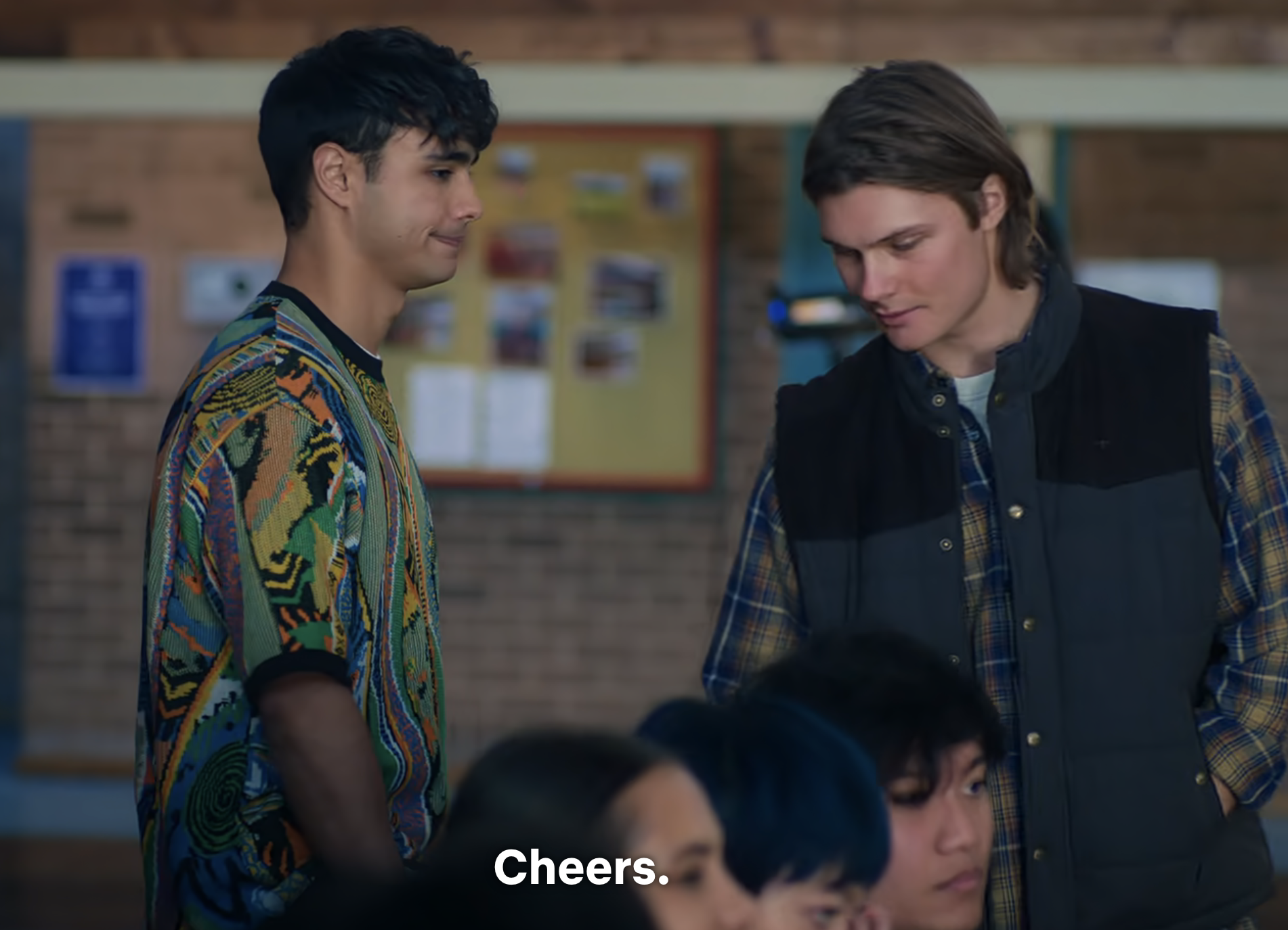 Two actors in a scene, one in a patterned shirt and the other in a plaid jacket, appearing to have a conversation