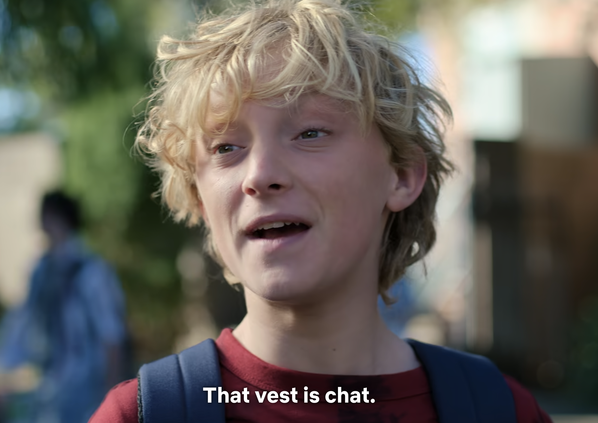 Boy with blond hair and a red backpack; subtitle reads &quot;That vest is chat.&quot;