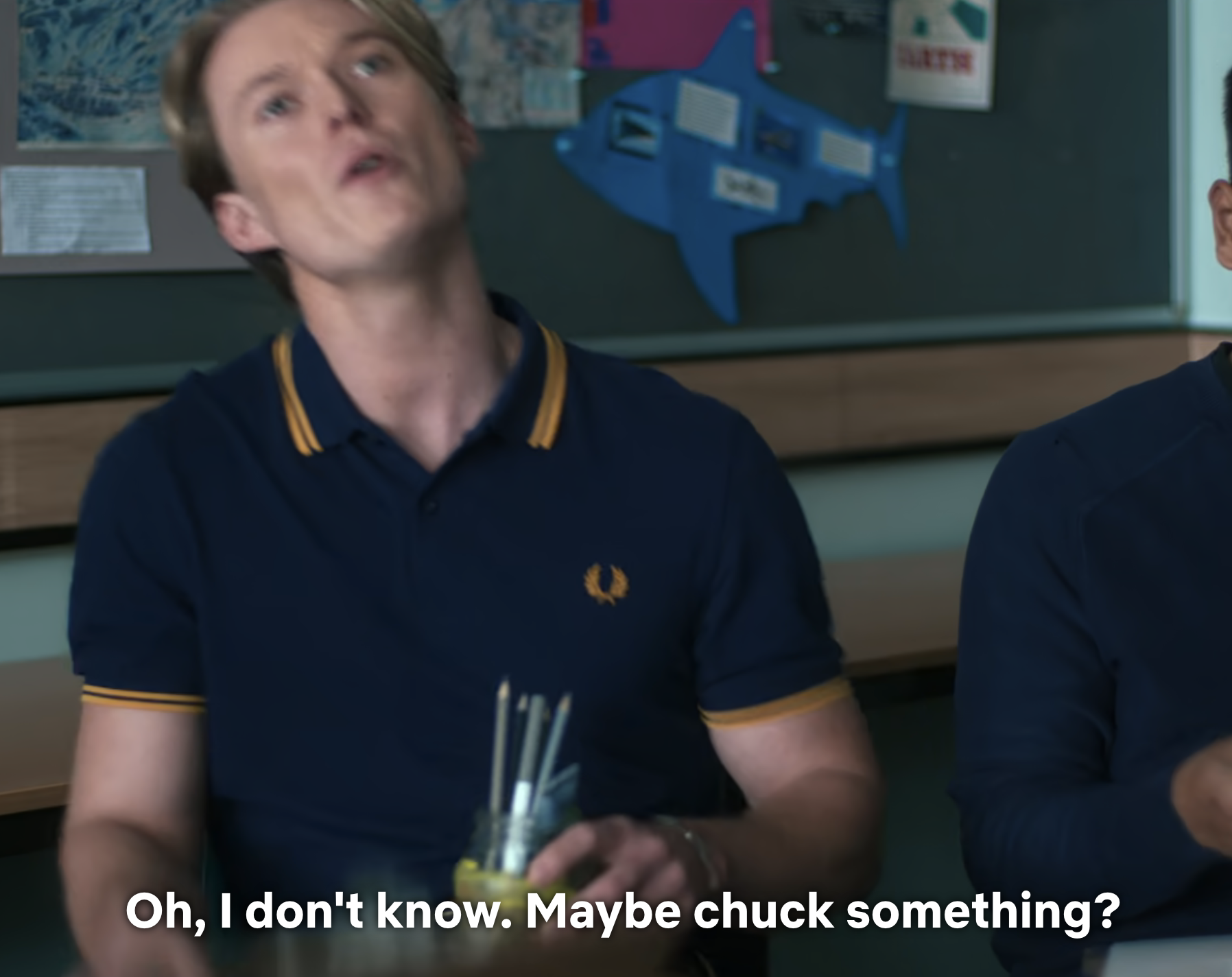 Two persons in a classroom, one gesturing with a puzzled expression and subtitles