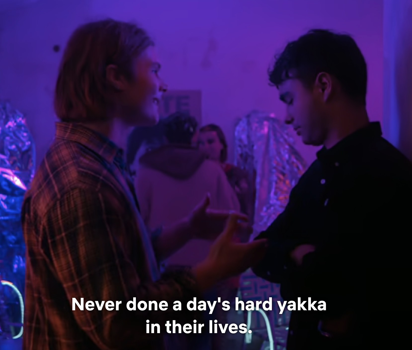 Two people engaged in a conversation in a dimly lit room with subtitles on the screen