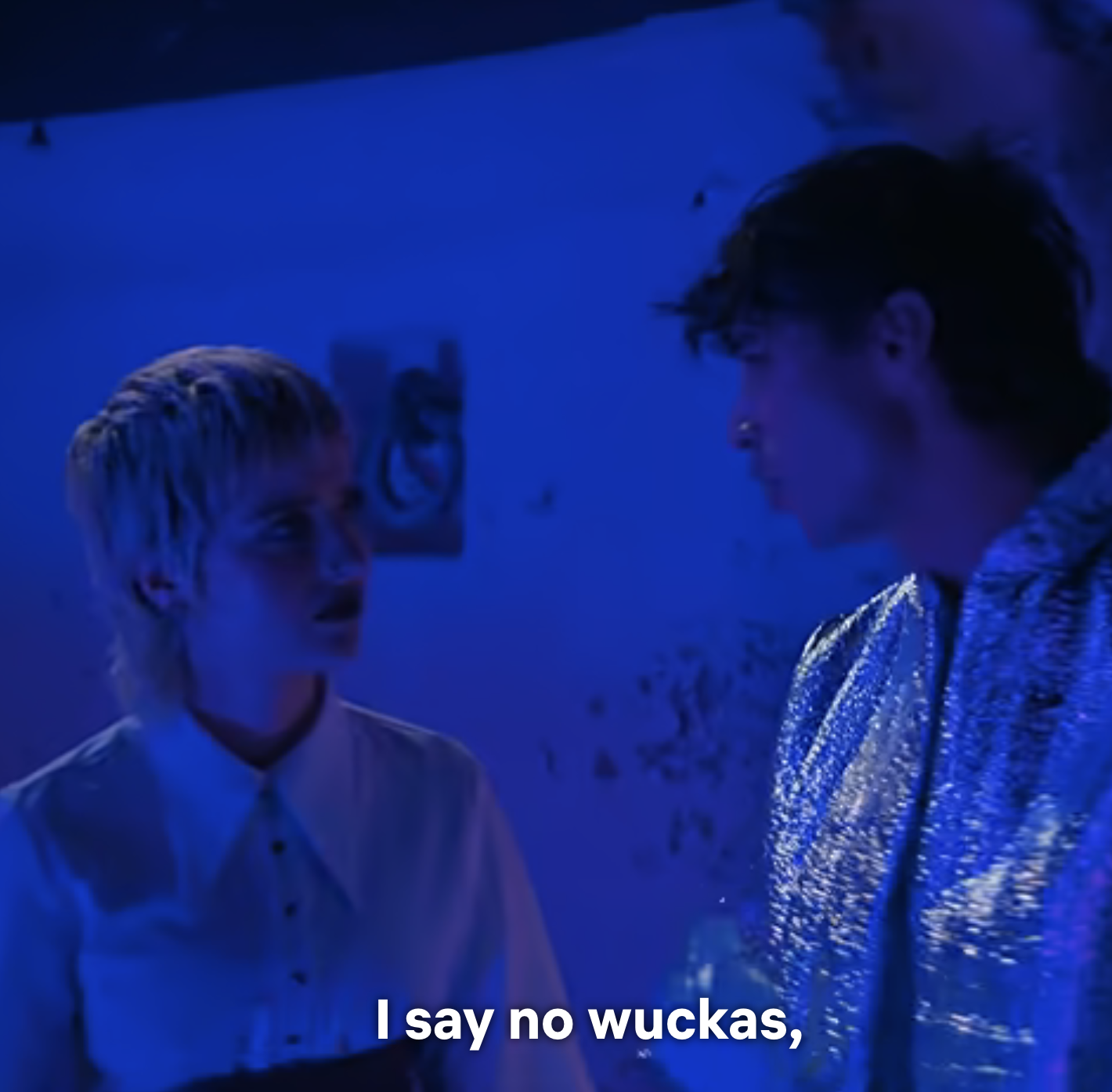 Two individuals in conversation under blue lighting with subtitle text &quot;I say no wuckas,&quot;