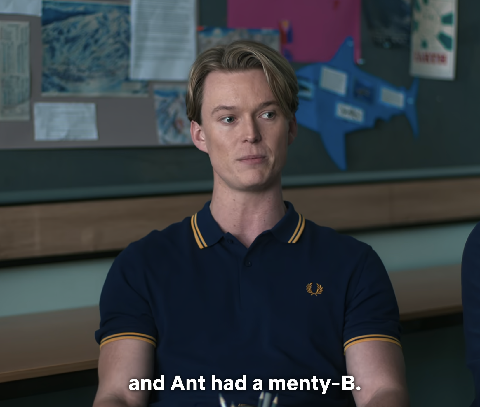 A person is wearing a polo shirt, sitting in a classroom, with a caption reading a slang phrase