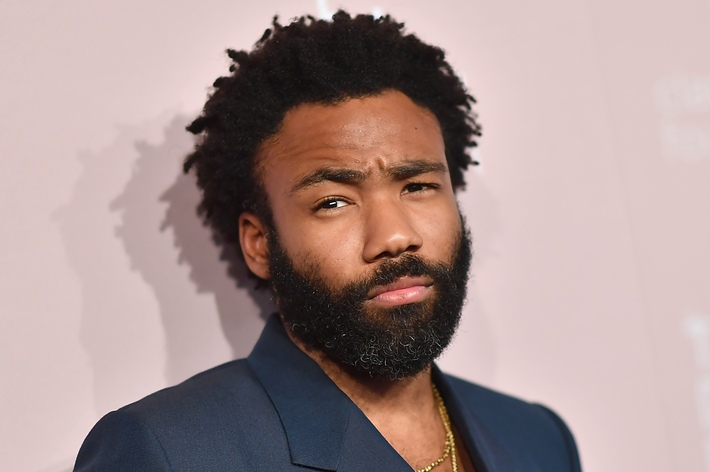 Donald Glover wearing a navy suit, looking serious at an event