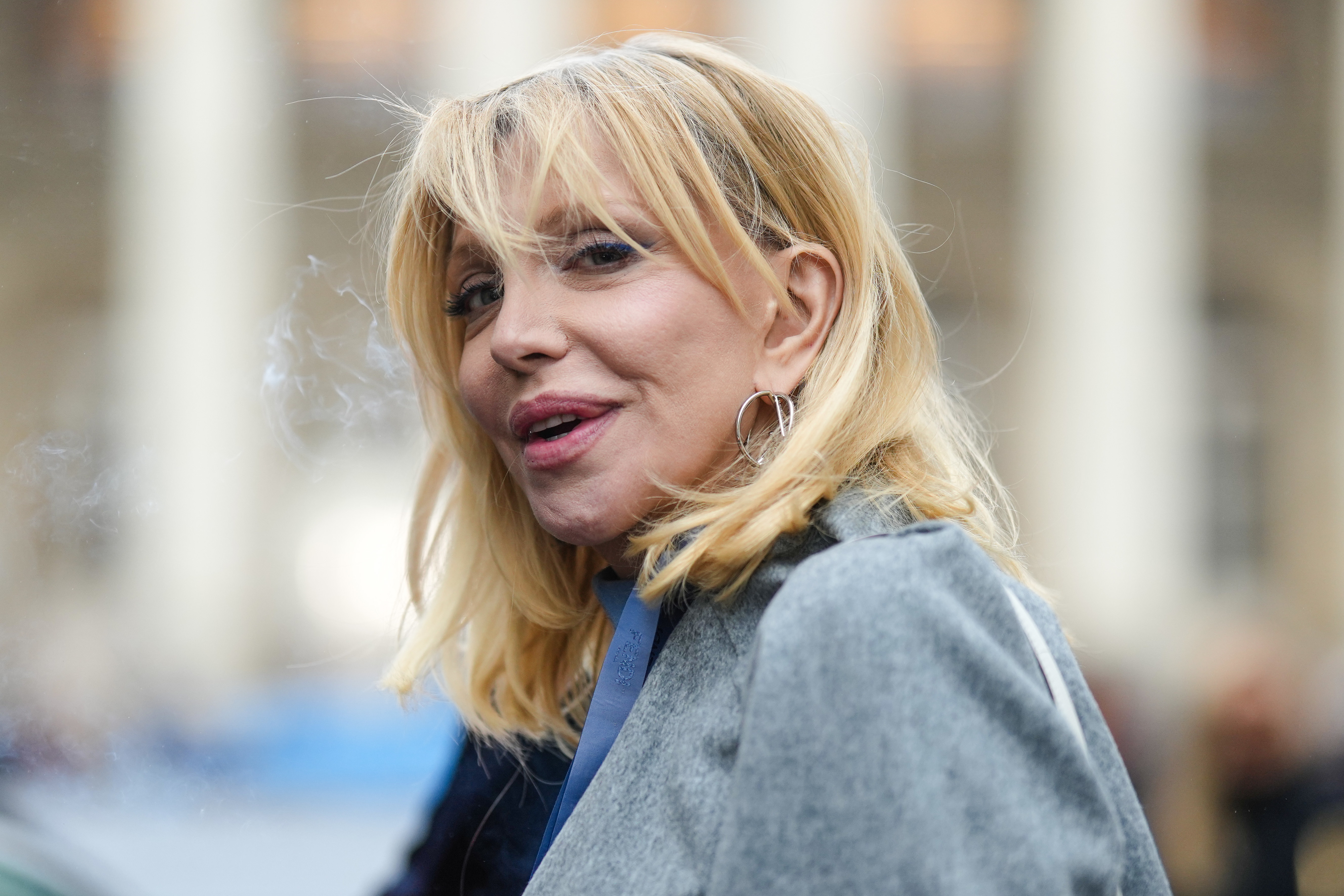 Courtney Love smiling outdoors while hoop earrings and a jacket