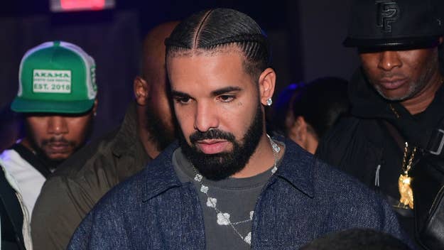 Drake in a denim jacket with a chain necklace, looking pensive at a night event
