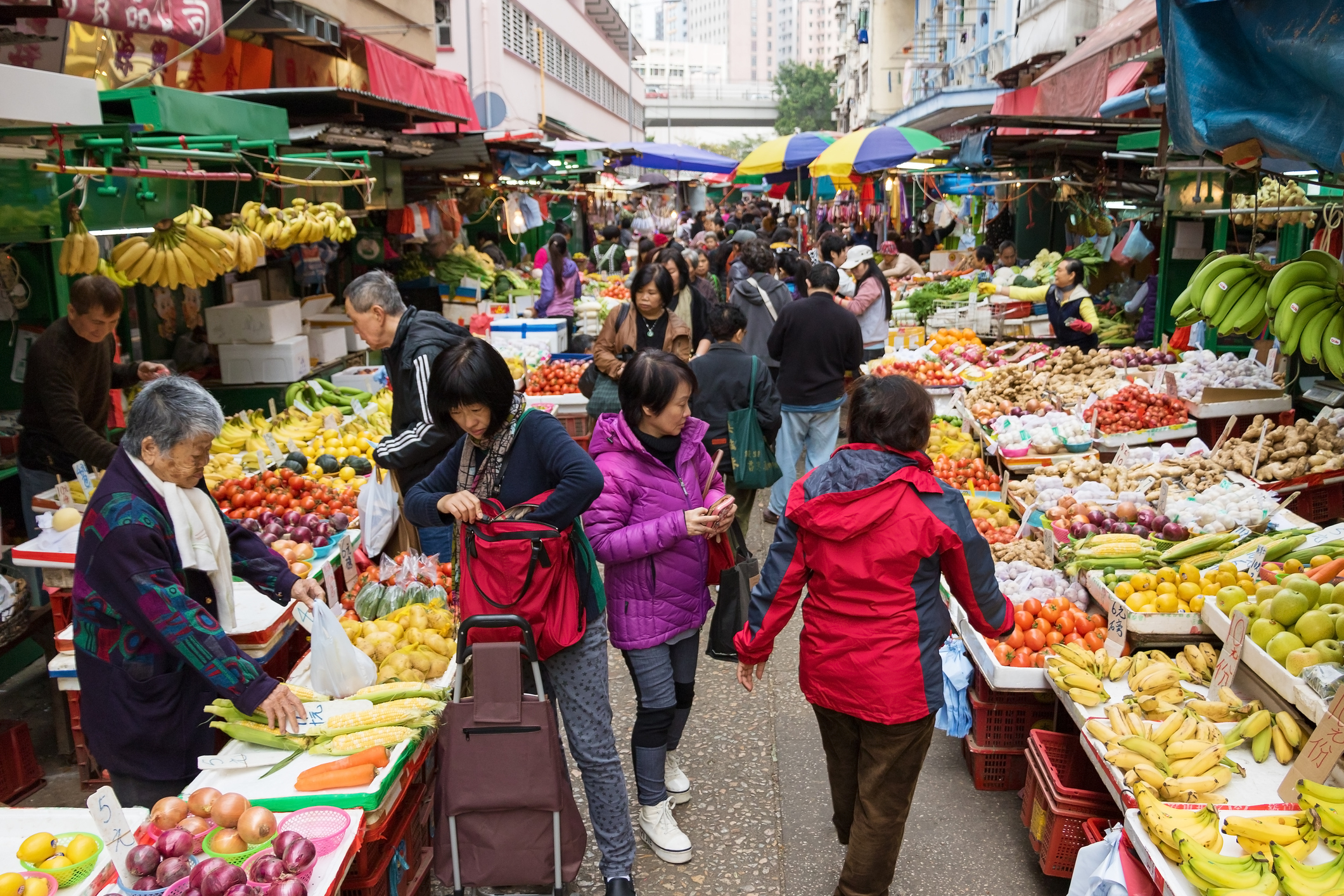 People shopping at a bustling outdoor fruit and vegetable market with various produce on display