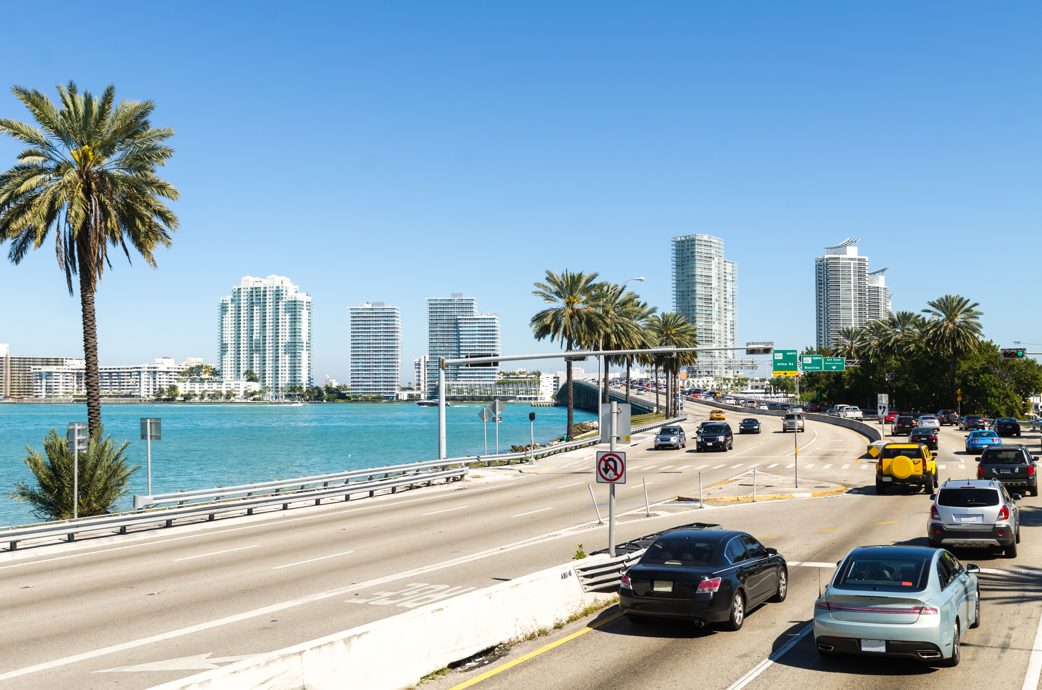 Skyline of Miami with buildings, palm trees, and vehicles on a highway by the water