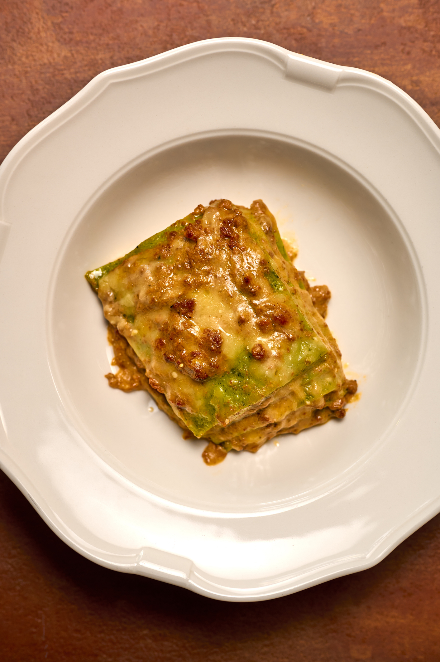 A slice of lasagna with melted cheese on a white plate